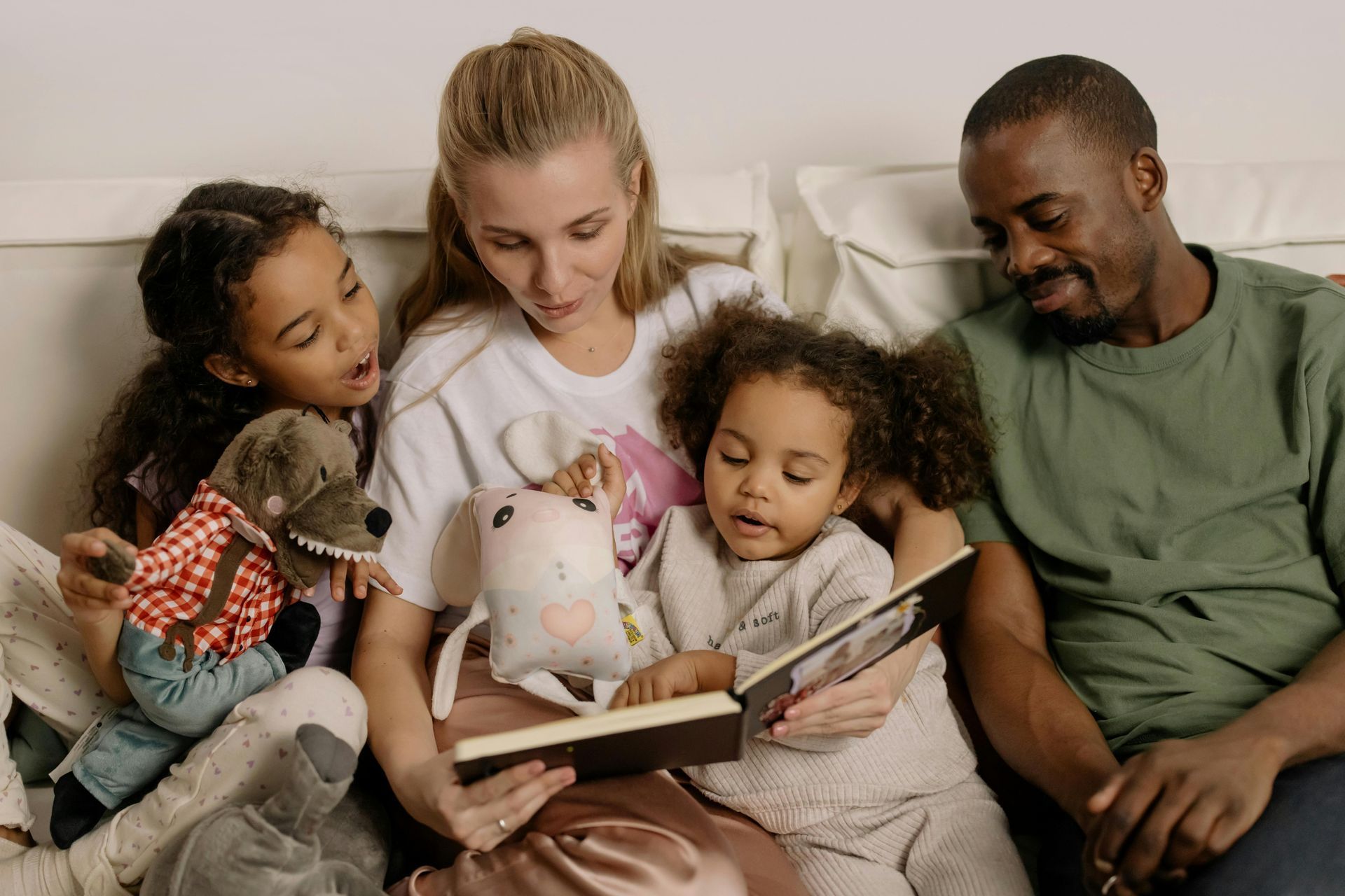 Family reading a book together on a couch, with stuffed animals.