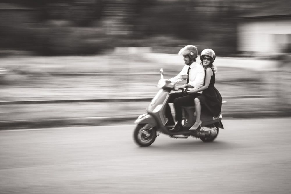 Zwei Personen fahren schnell mit einem Roller durch eine verschwommene Stadtstraße