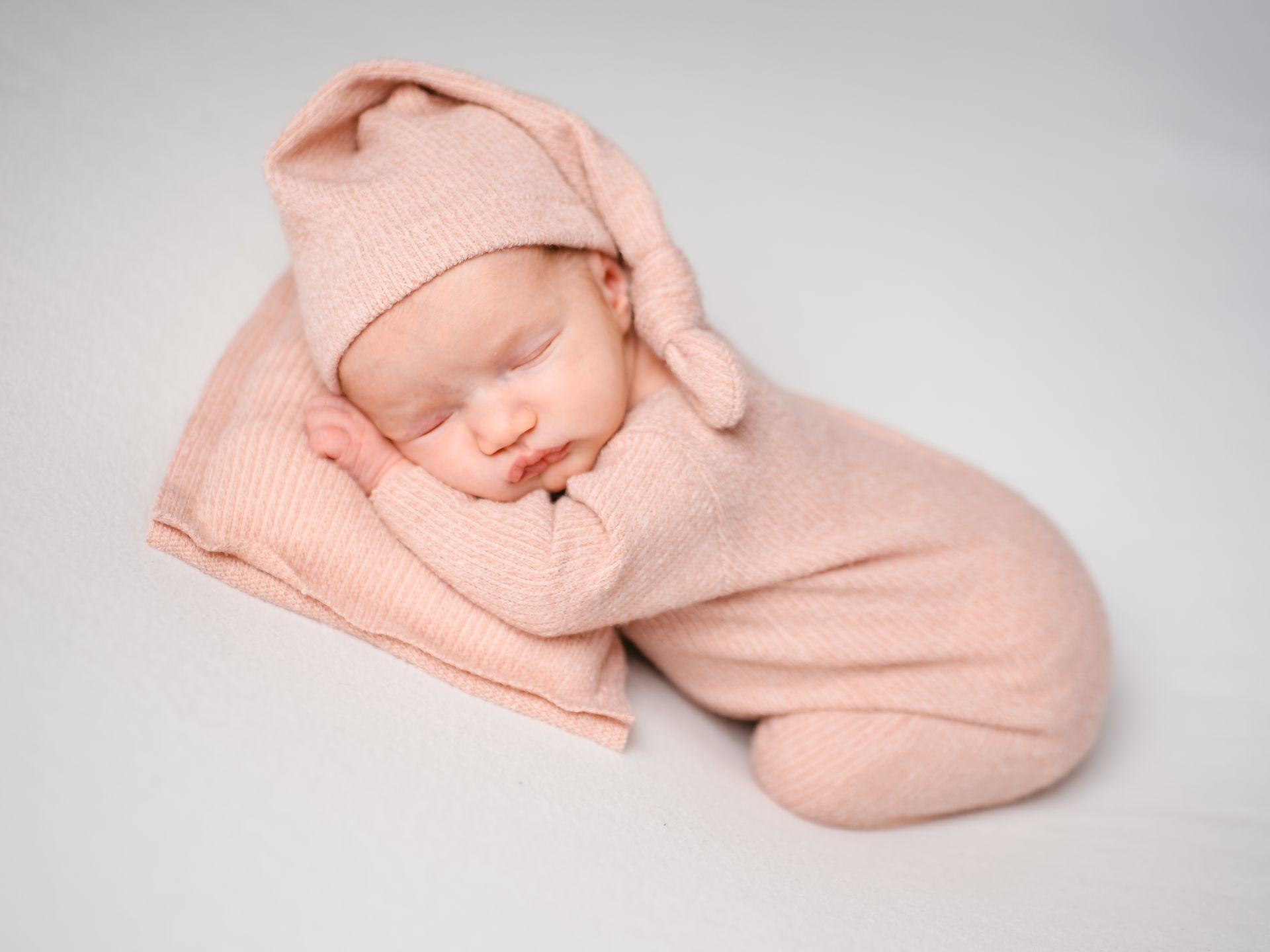 Schlafendes Baby, eingewickelt in eine weiche rosa Decke und passende Mütze, vor hellem Hintergrund