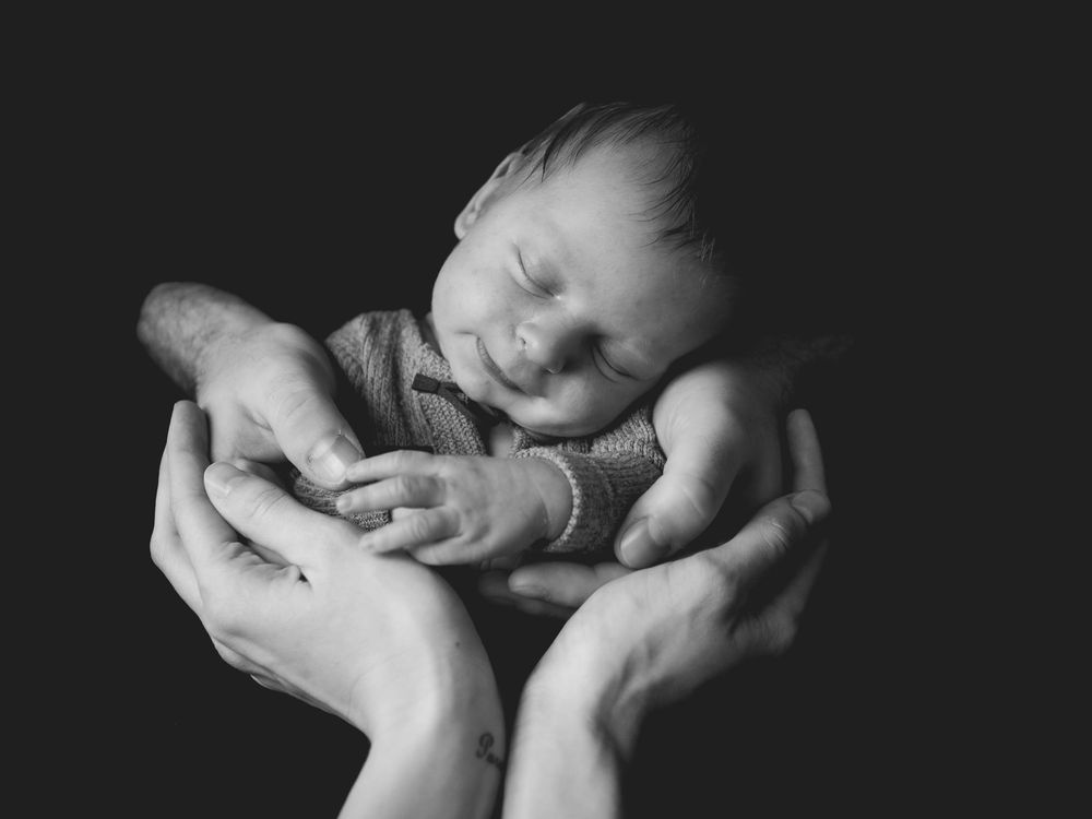 Schlafendes Baby, gehalten von zwei Erwachsenenhänden, in Schwarzweiß.