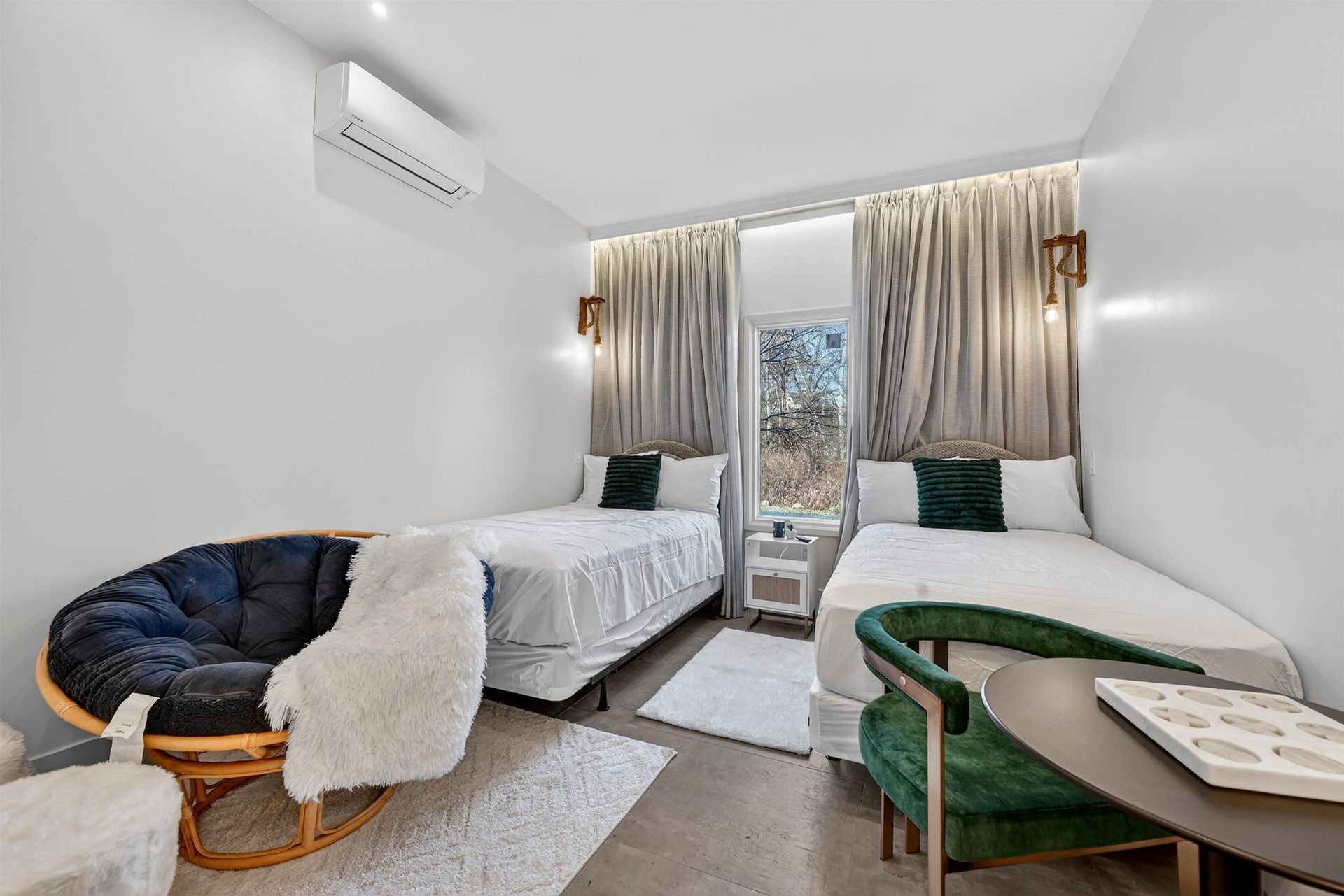 Small bedroom with two twin beds, a window, and two chairs in a bright, white room.