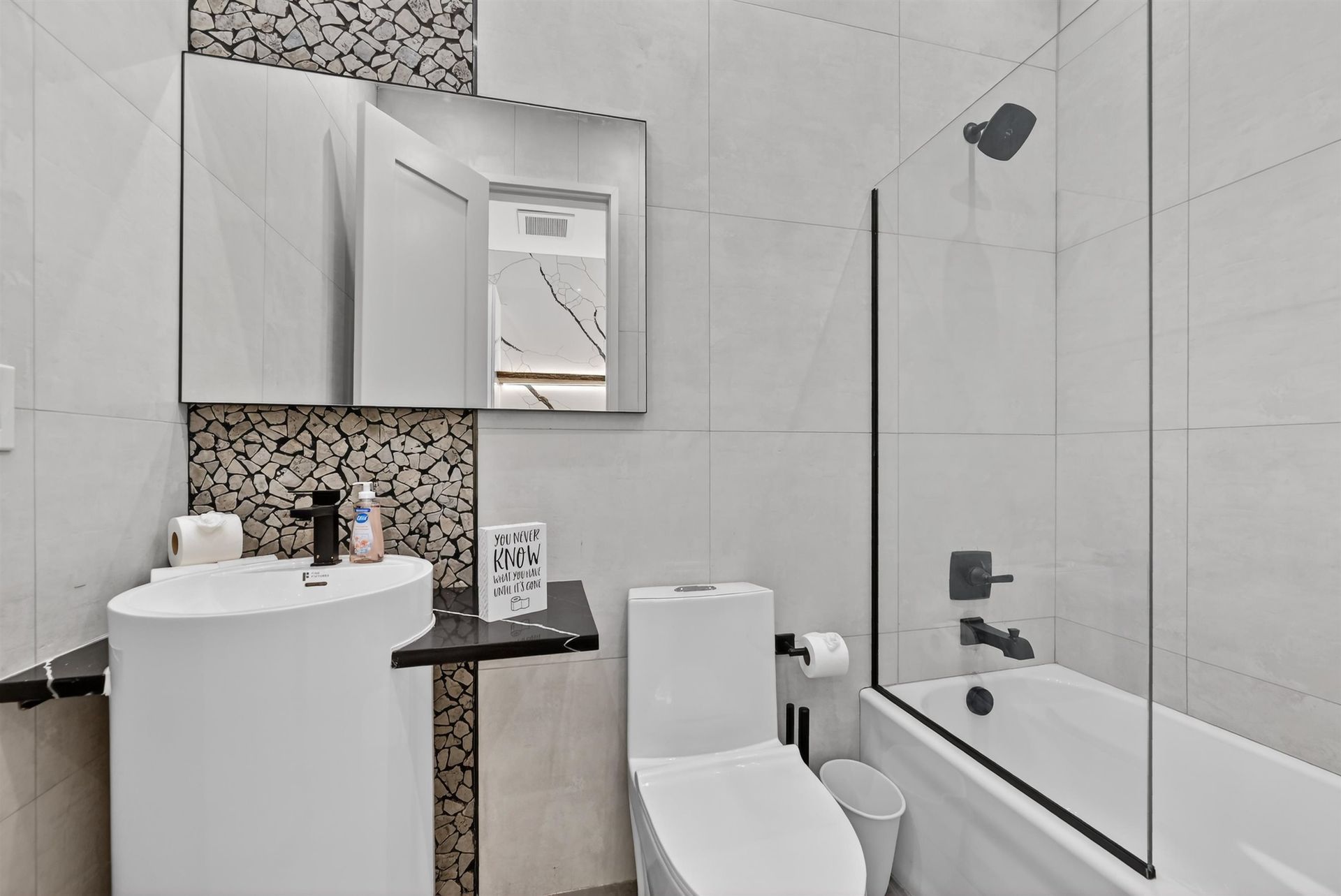 Compact modern bathroom with white tiles, vanity, toilet, mirror cabinet, and bathtub with glass screen