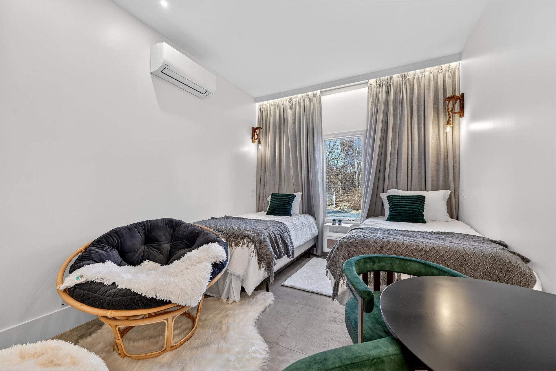 Bright bedroom with two beds, a round chair, and curtains by a large window