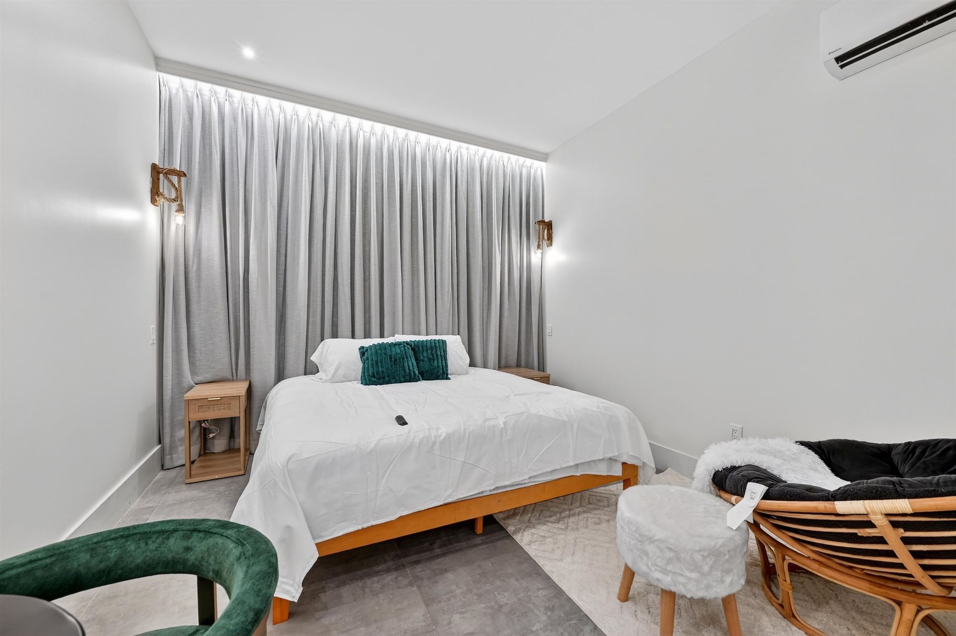 Bright bedroom with a white bed, gray curtains, green chair, and small wooden side tables