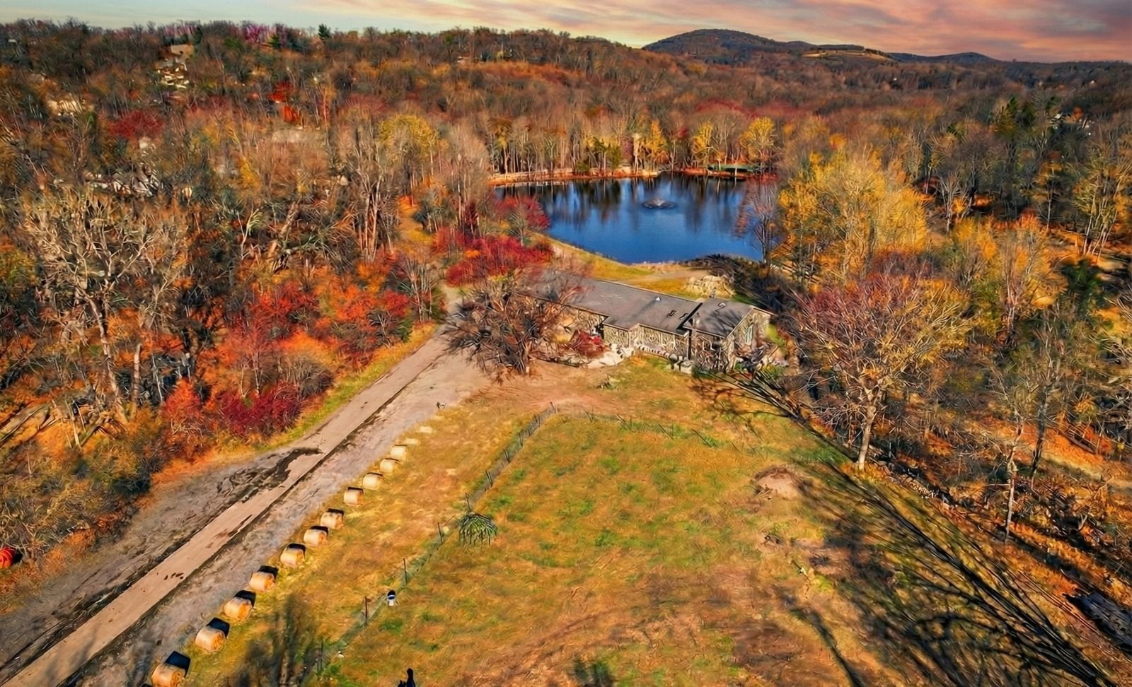 Autumn aerial view of a small blue pond beside a grassy field and forested hills