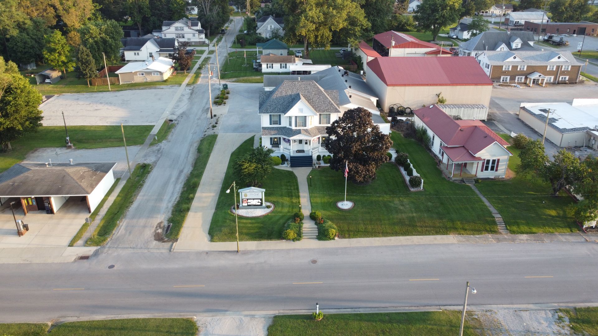 Aerial view of a suburban street with houses, lawns, trees, and a road in the foreground
