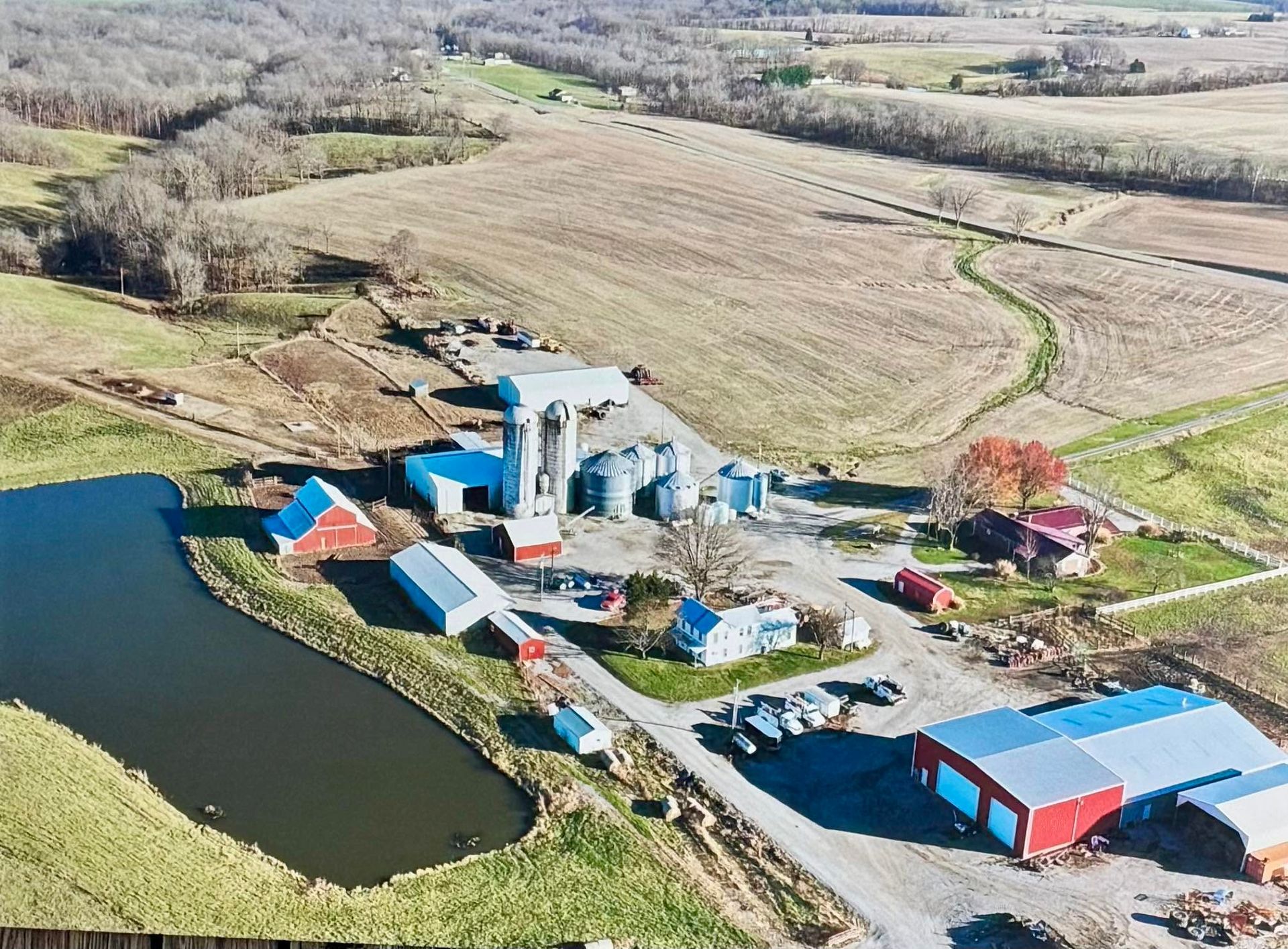 Aerial view of a rural farm by a pond, with silos, barns, and fields in winter