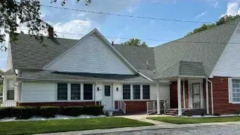 Single-story suburban house with white siding, gray roof, and red brick accents under a cloudy sky