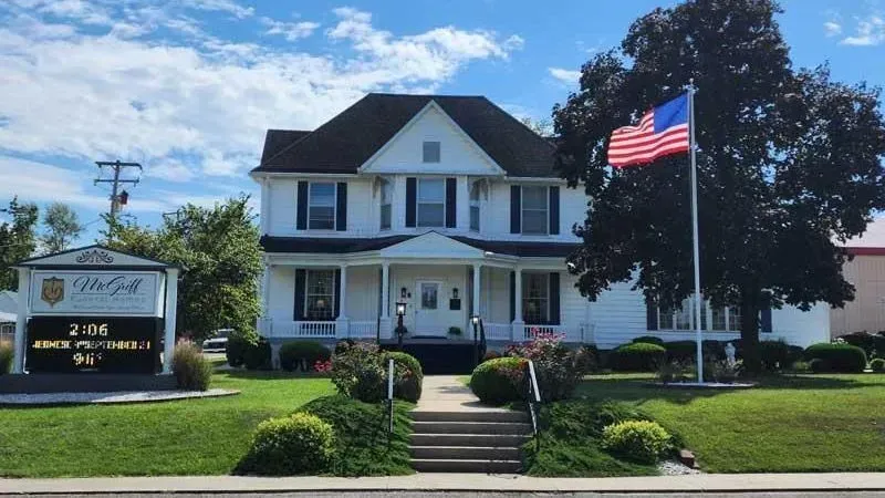 White colonial-style house with an American flag and a sign in front on a sunny day