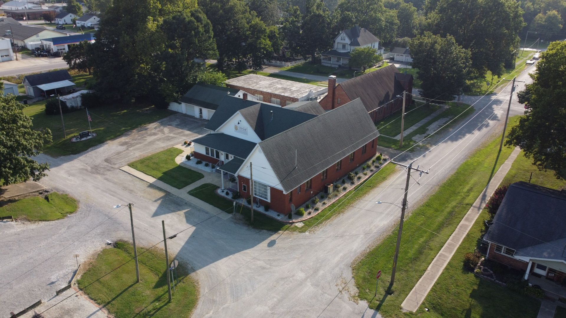 Aerial view of a red brick church and white house at a quiet rural street intersection.