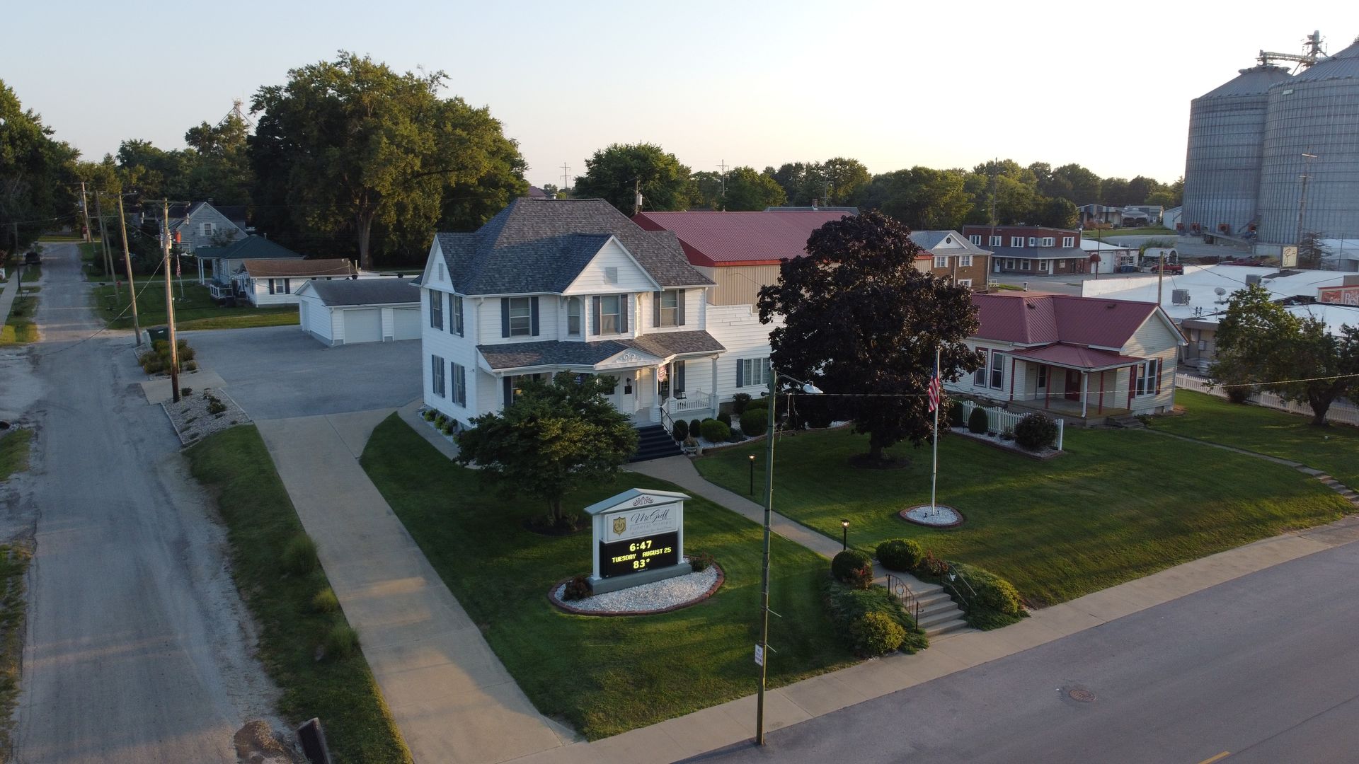 Aerial view of a residential street with houses, lawns, trees, and a roadside sign at dusk