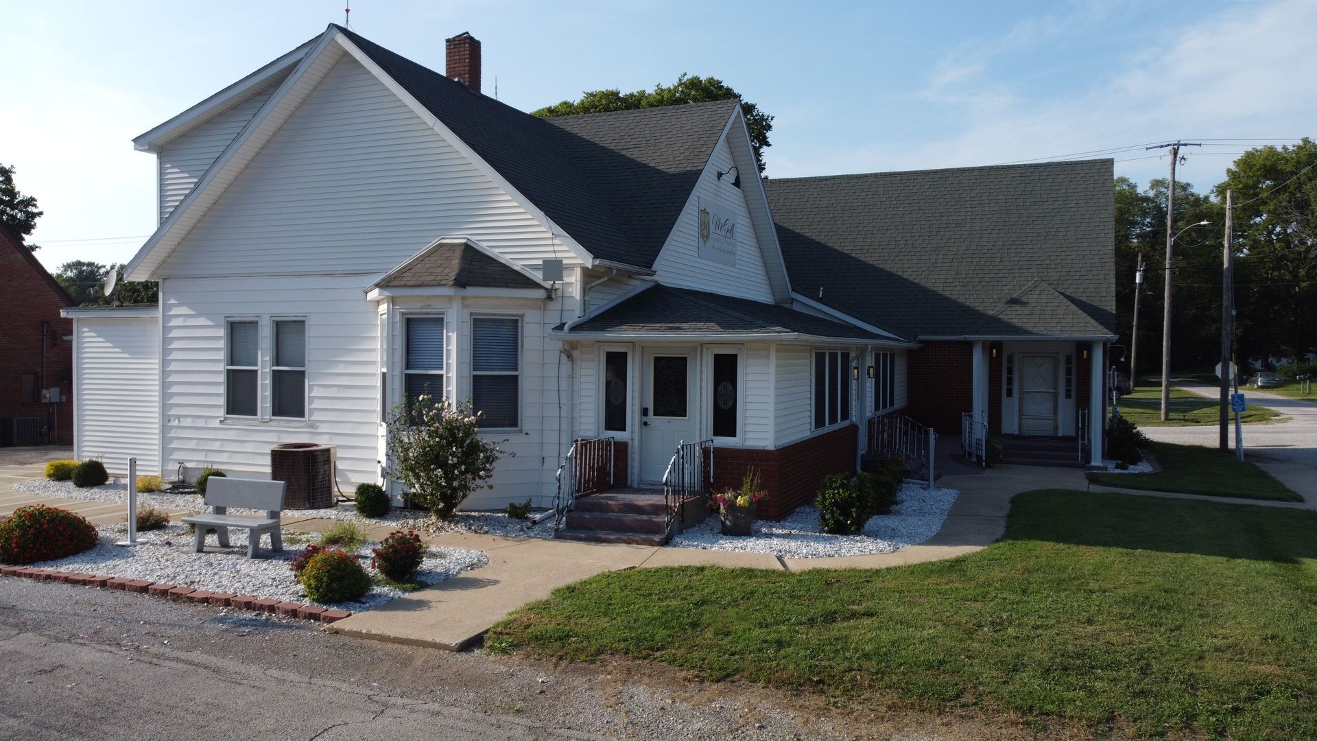 White house with porch and landscaped front yard on a sunny street corner