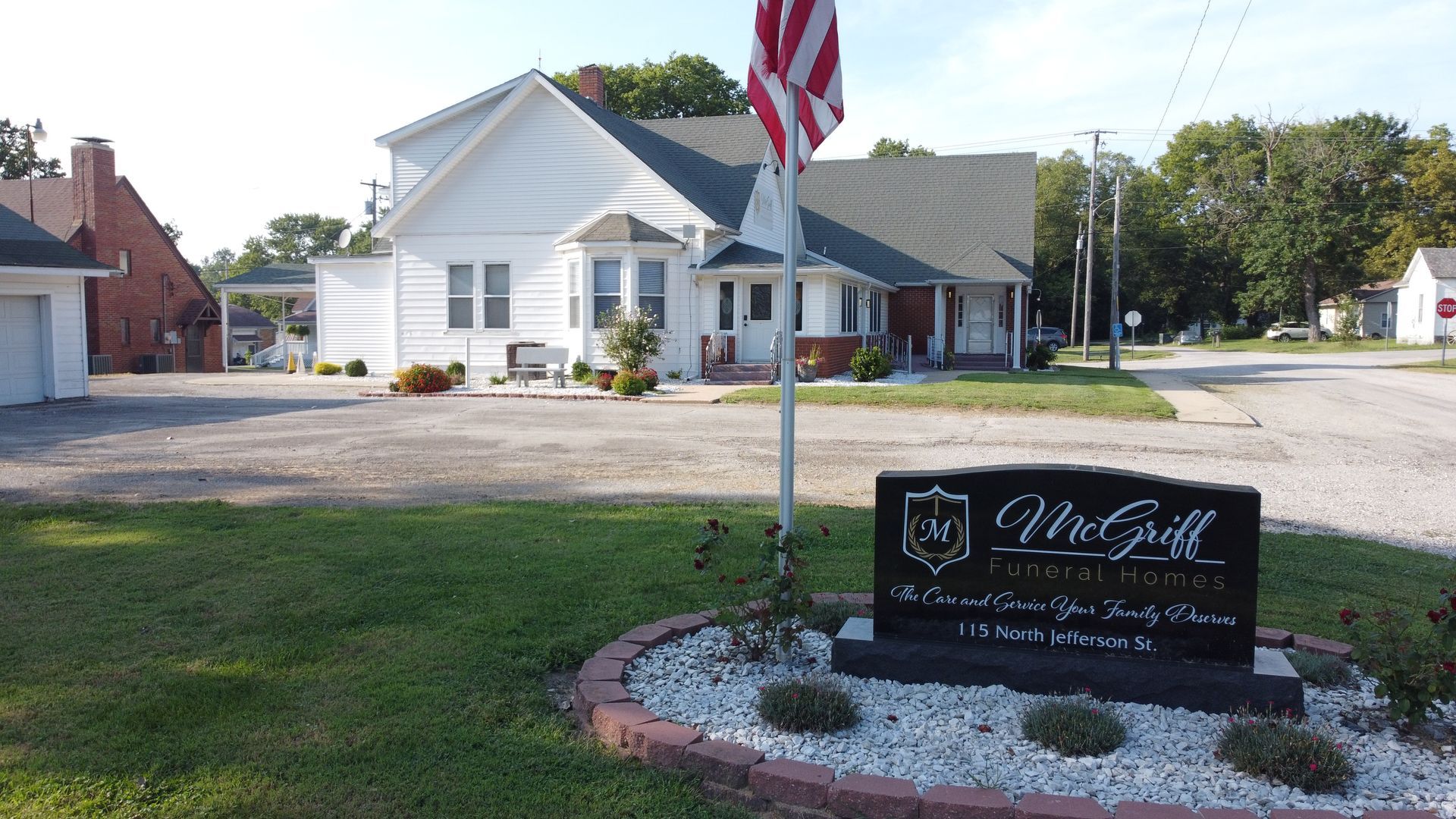 White house with an American flag and a black memorial sign in the front yard.