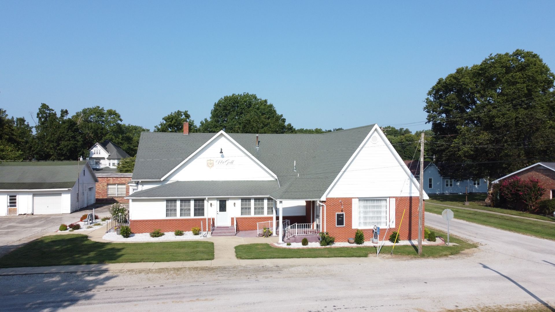 Single-story brick building with white gables and a gray roof beside a parking lot and lawn