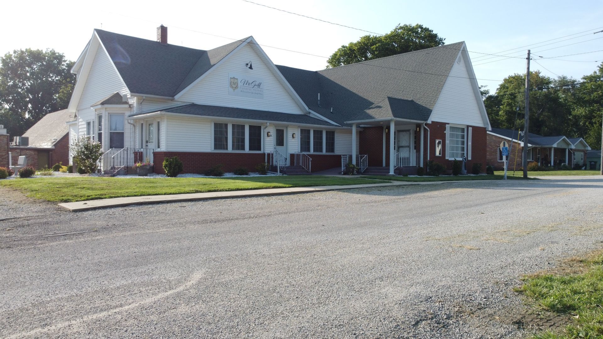 White church building with a red brick base beside a gravel road on a sunny day