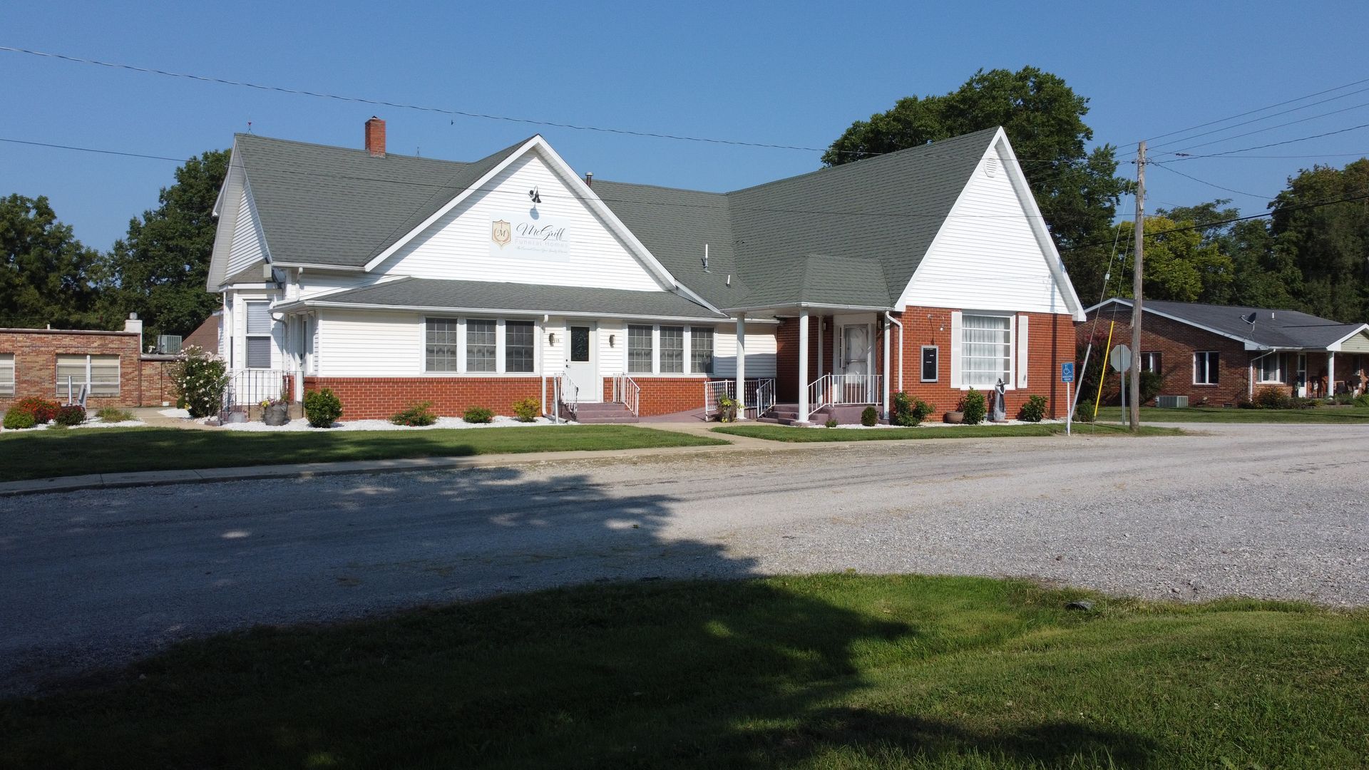 White house with red-brick accents and a gravel driveway under a clear blue sky.