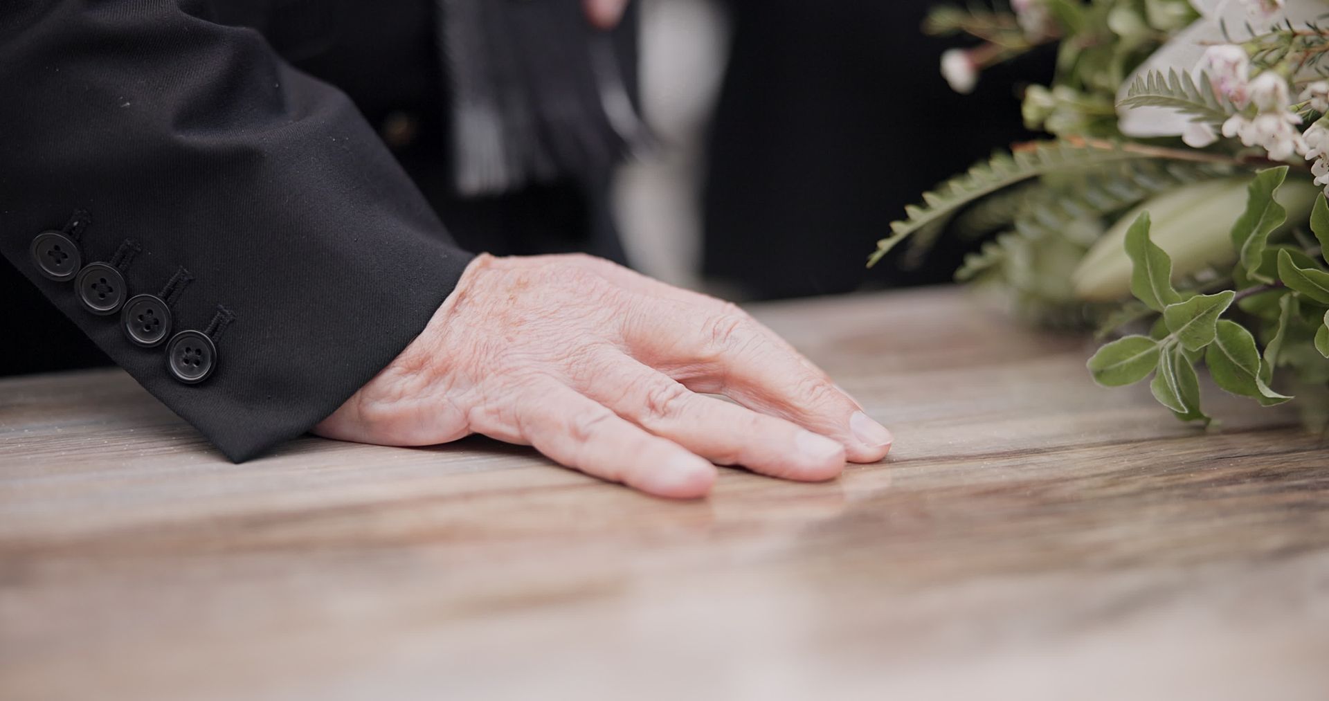 A man in a suit is sitting at a coffin at a funeral.