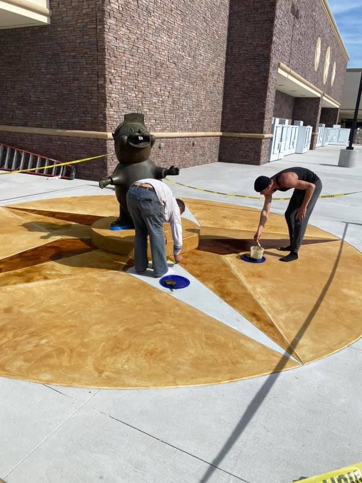 Two men are painting a statue outside of a building.