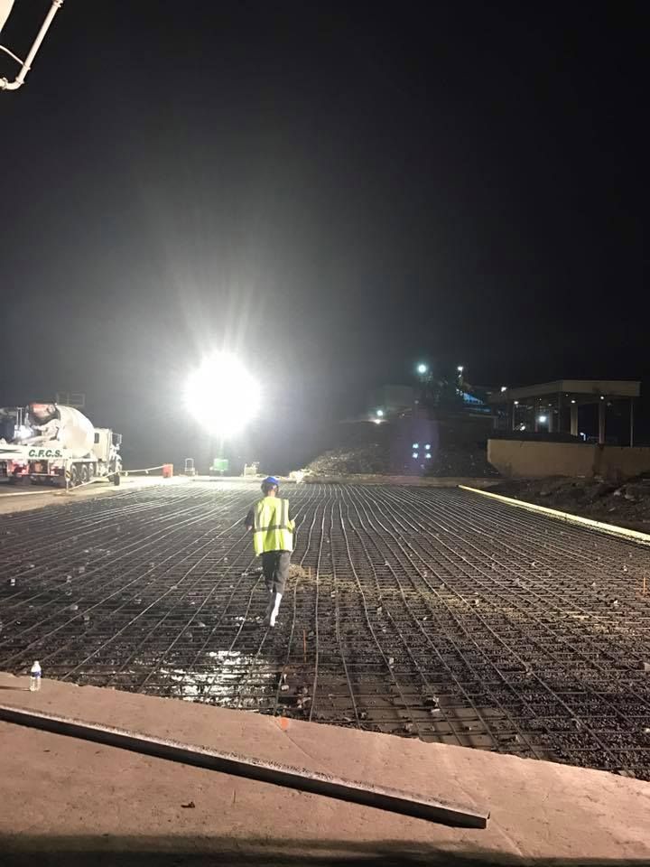 A man in a yellow vest is walking on a construction site at night.