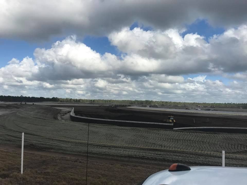 A white truck is parked in front of a dirt field with clouds in the sky.
