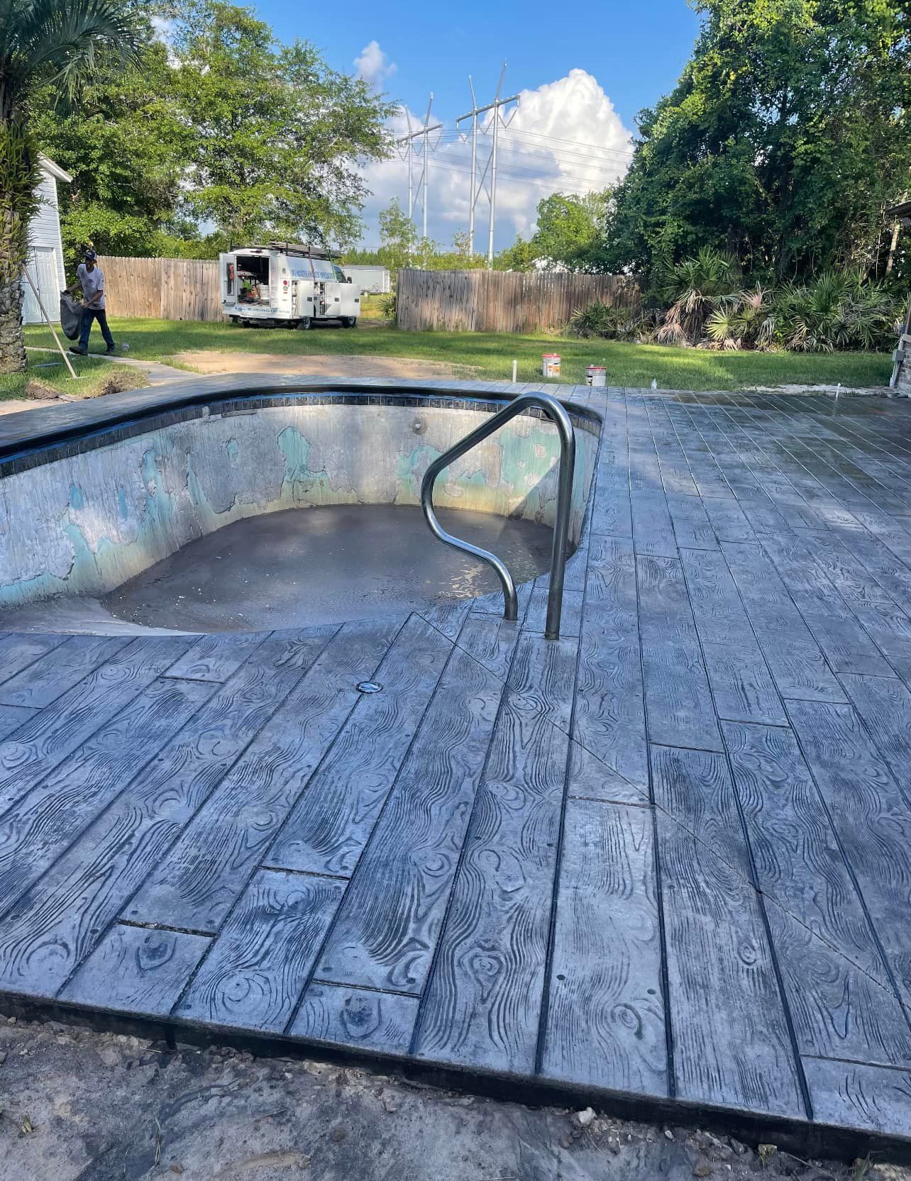A concrete deck next to a swimming pool with a railing.