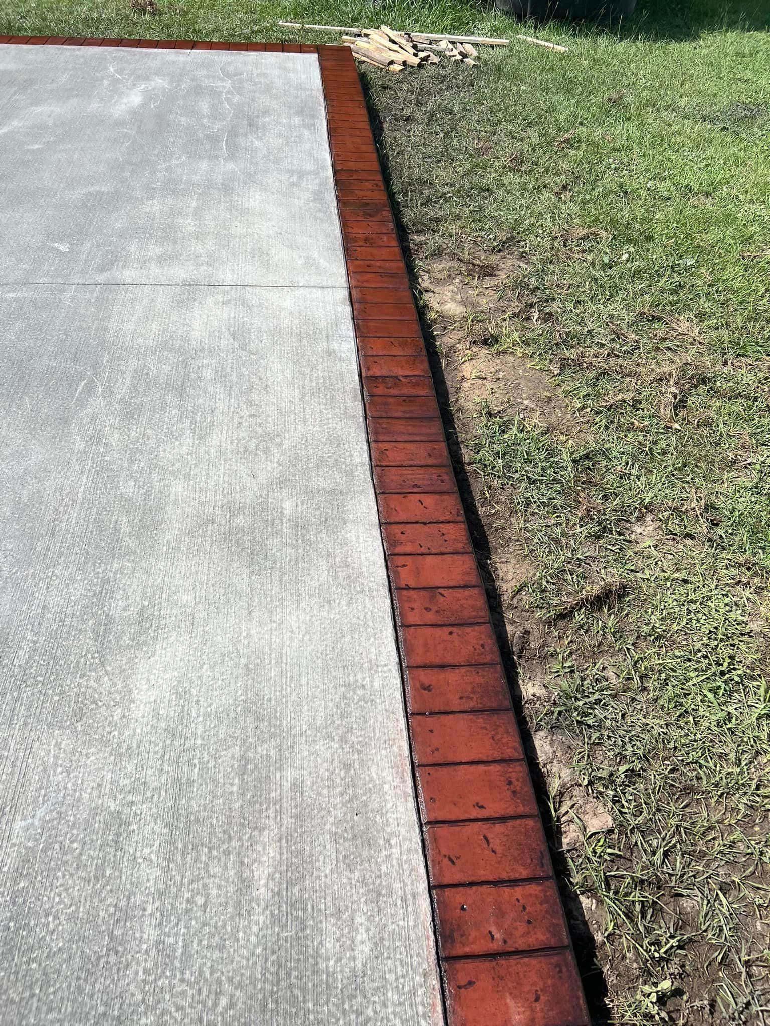 A concrete driveway with a red brick border and grass in the background.