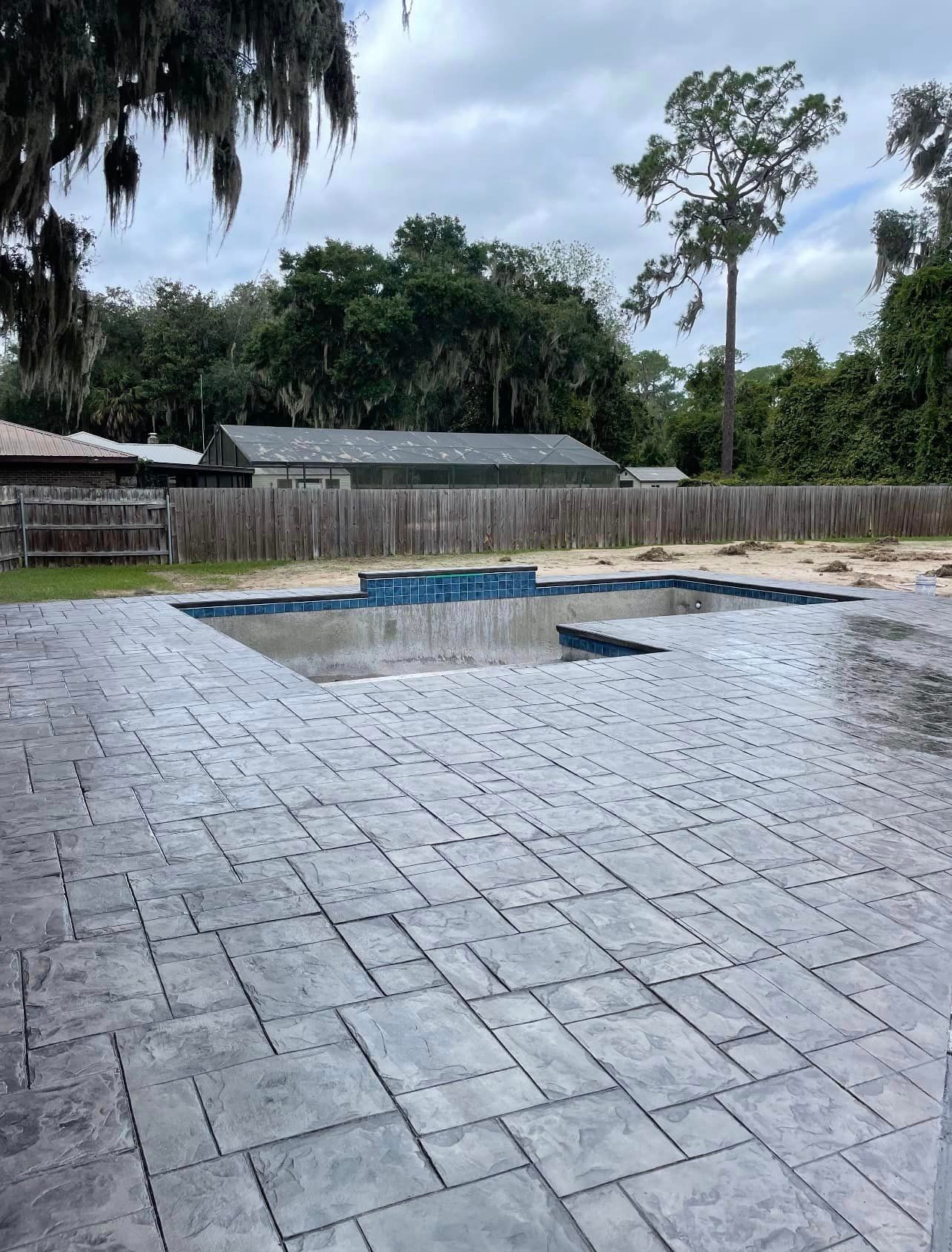 A patio with a pool in the background and a fence in the background.