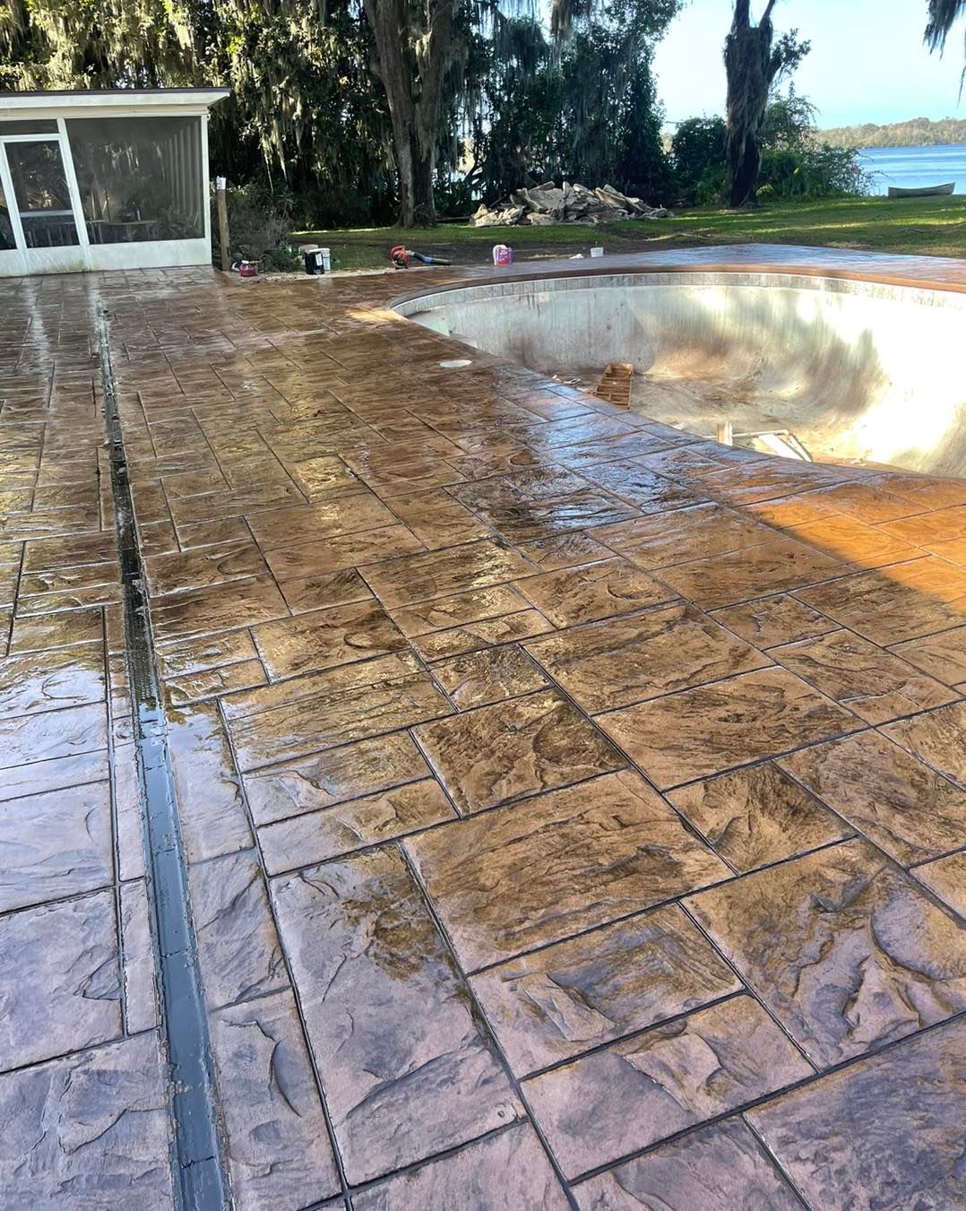 A concrete patio next to a swimming pool with a house in the background.