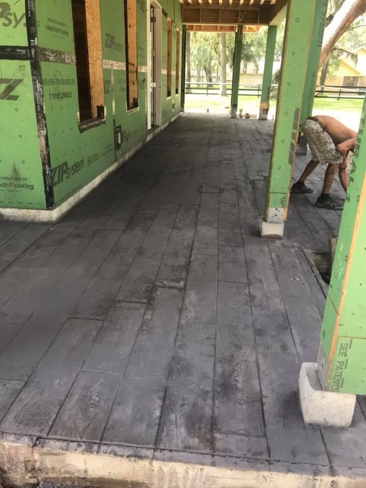 A man is working on a concrete walkway under a covered porch