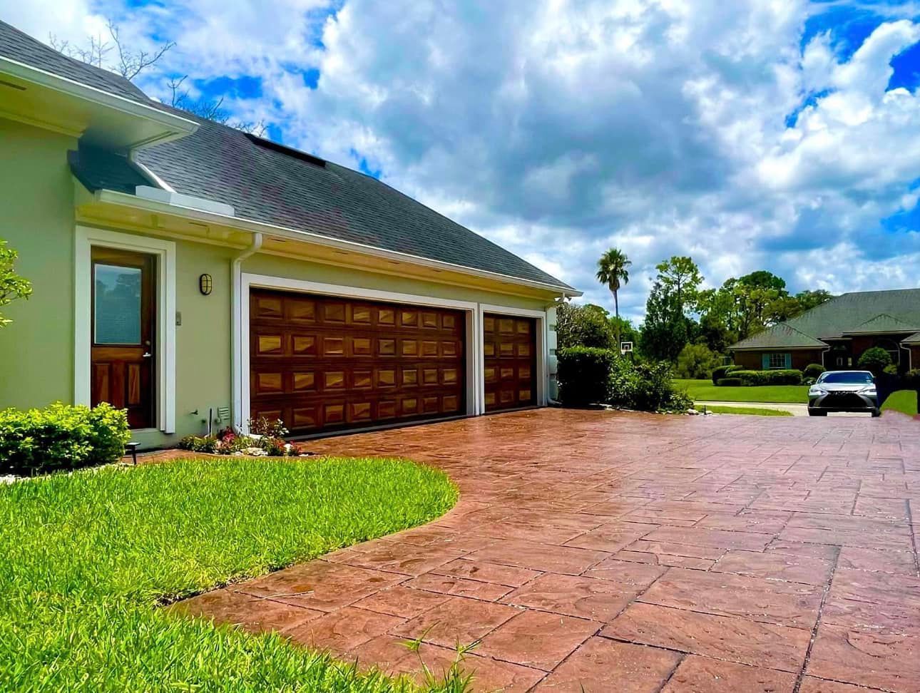A car is parked in front of a house with two garage doors.