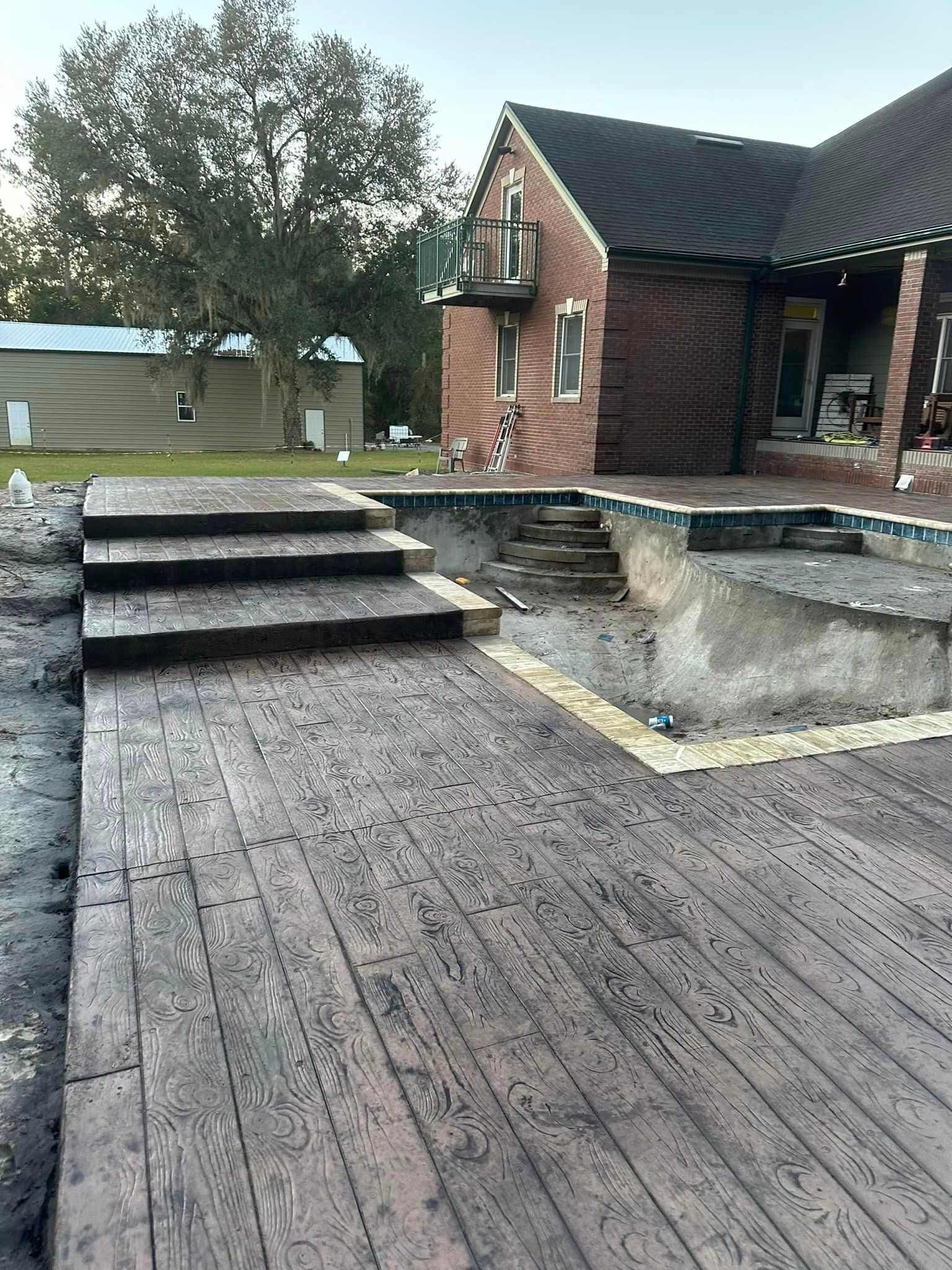 A wooden deck with stairs leading to a swimming pool in front of a brick house.
