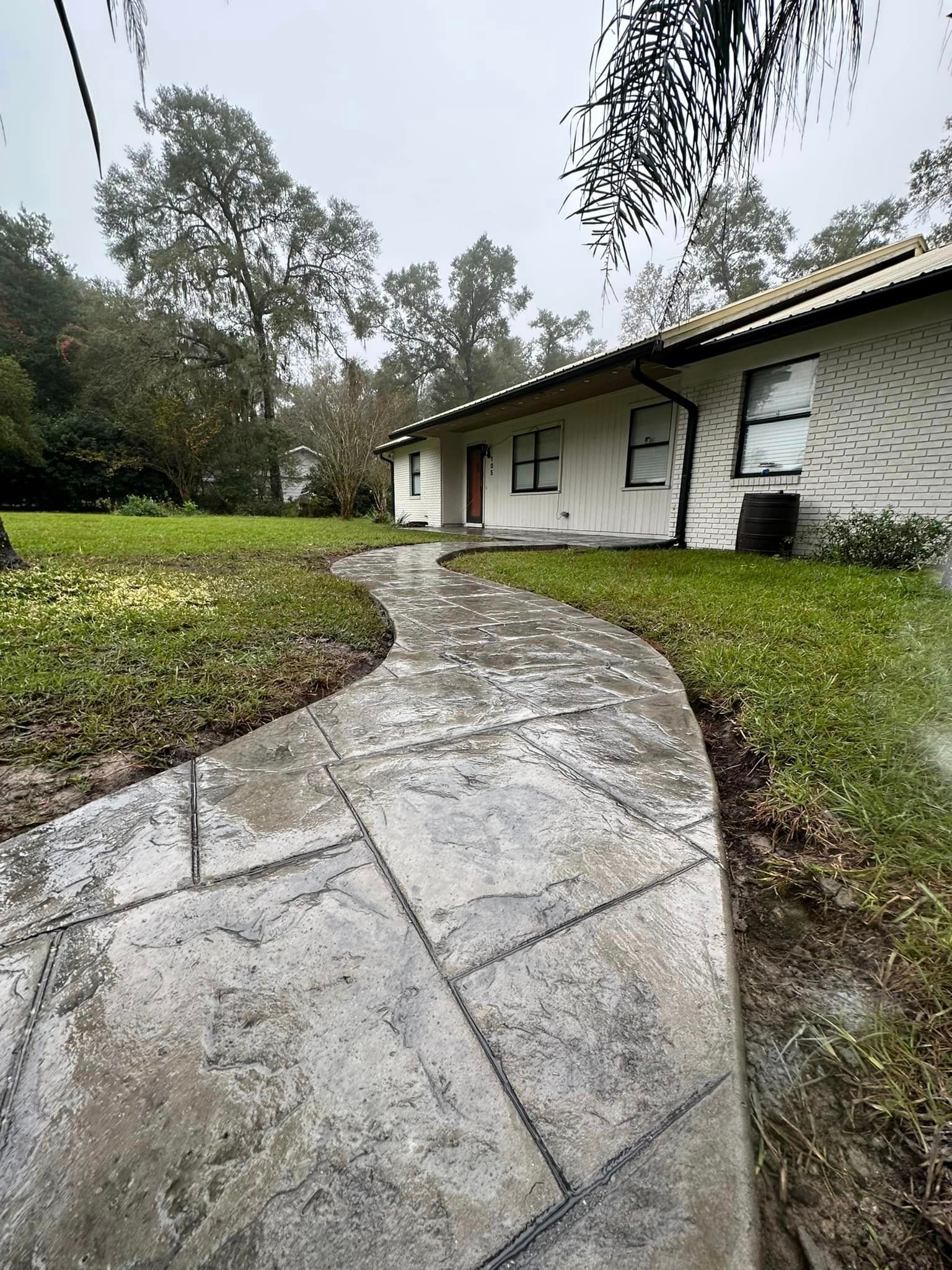 A concrete walkway leading to a white house in the rain.
