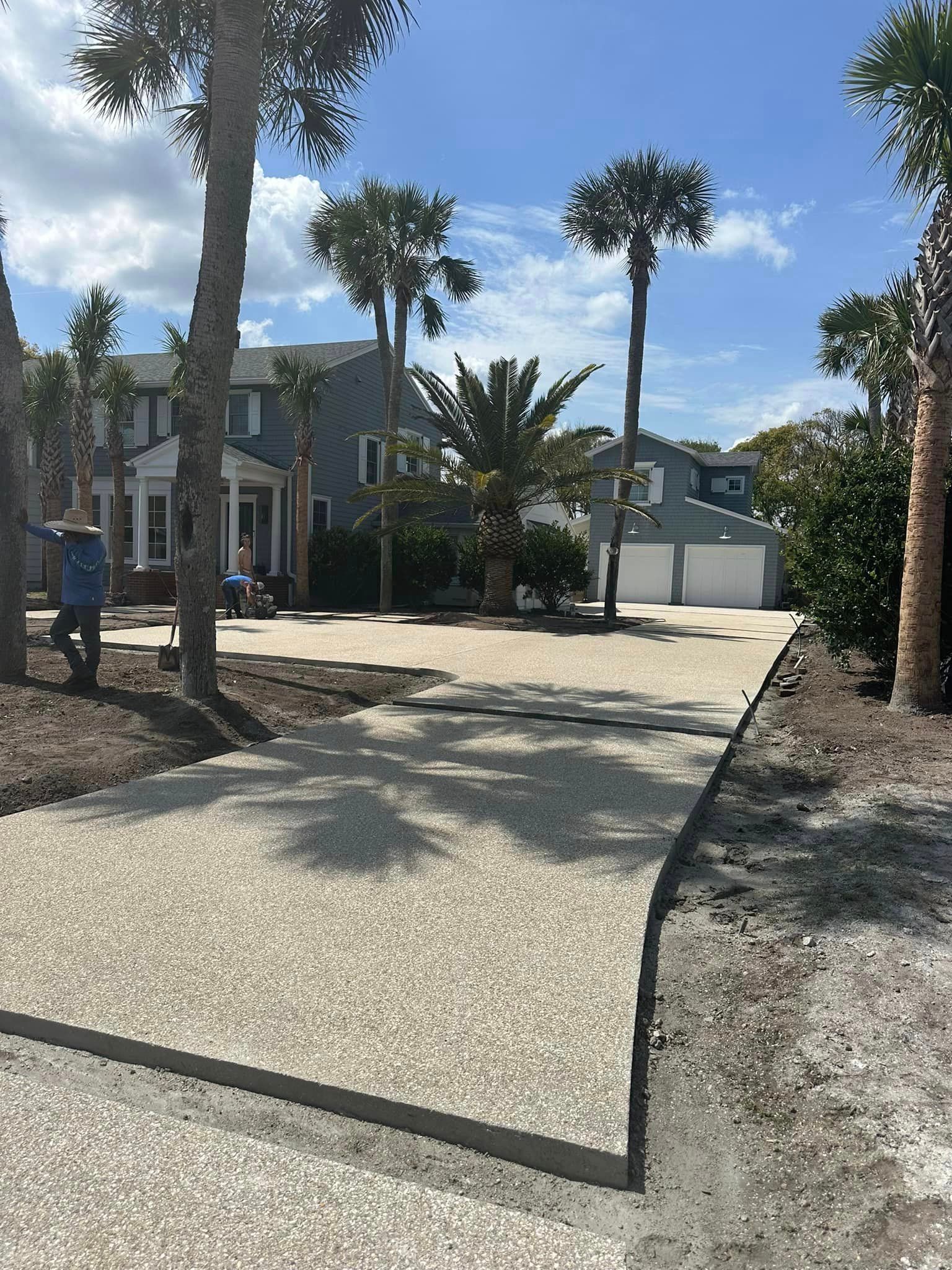 A concrete driveway is being built in front of a house with palm trees.
