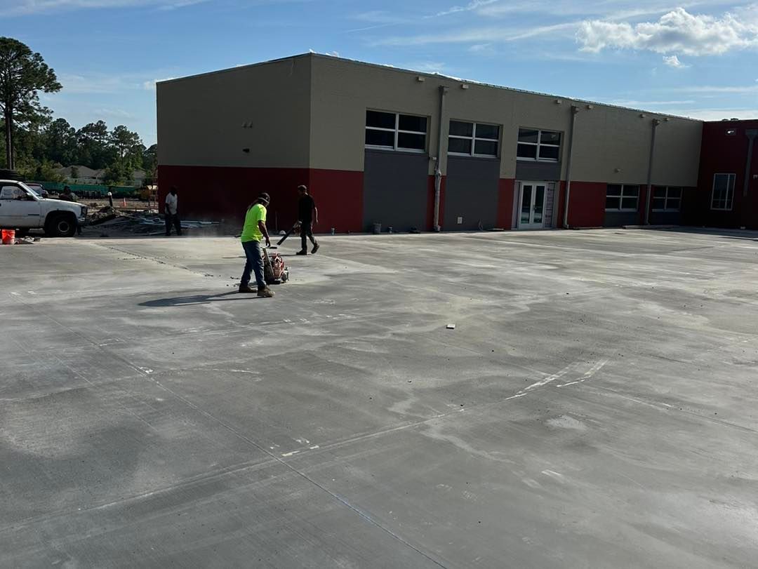 A man is grinding concrete in a parking lot in front of a building.