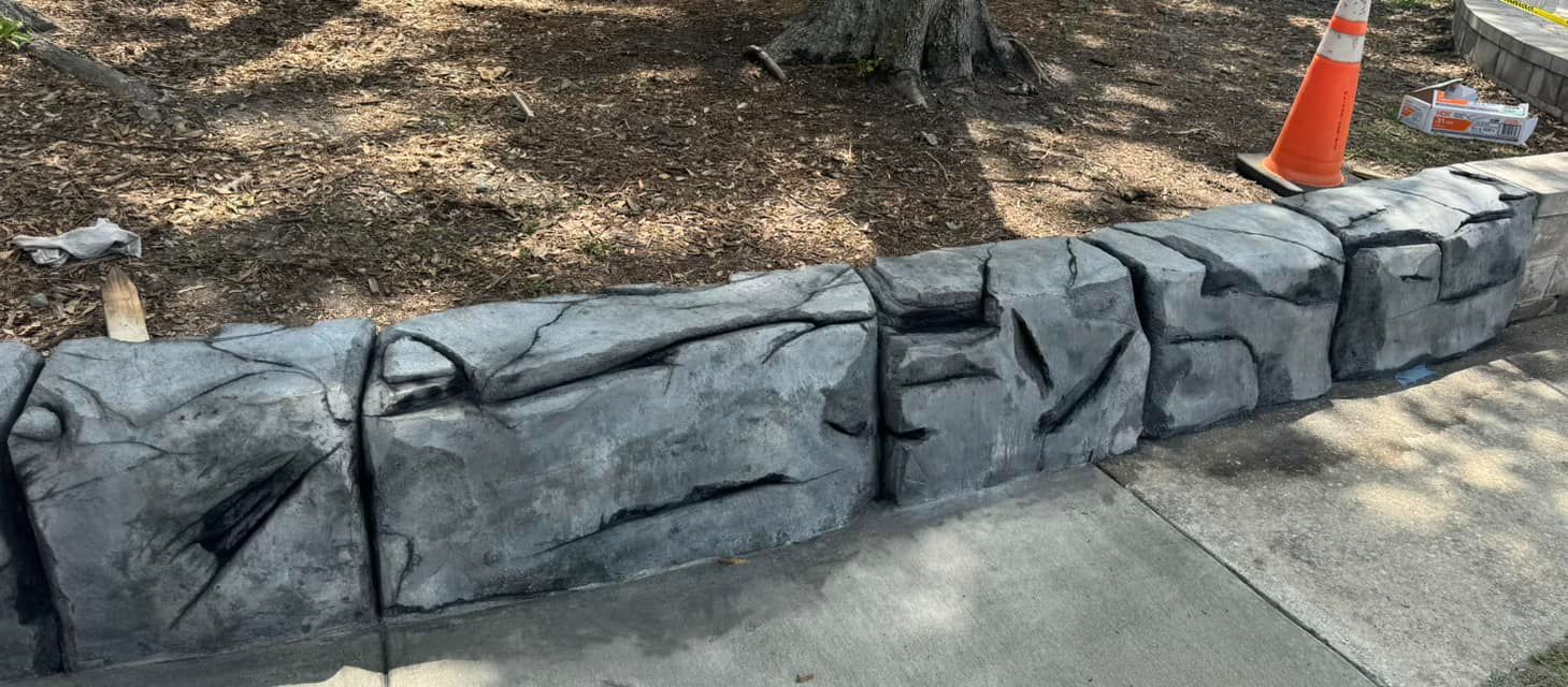 A large rock is sitting on the sidewalk next to a tree.