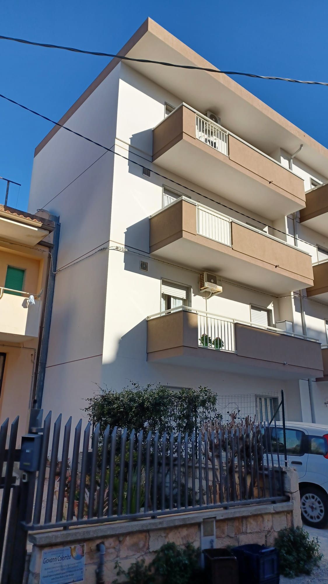 Moderno condominio con balconi beige dietro una recinzione su una strada soleggiata