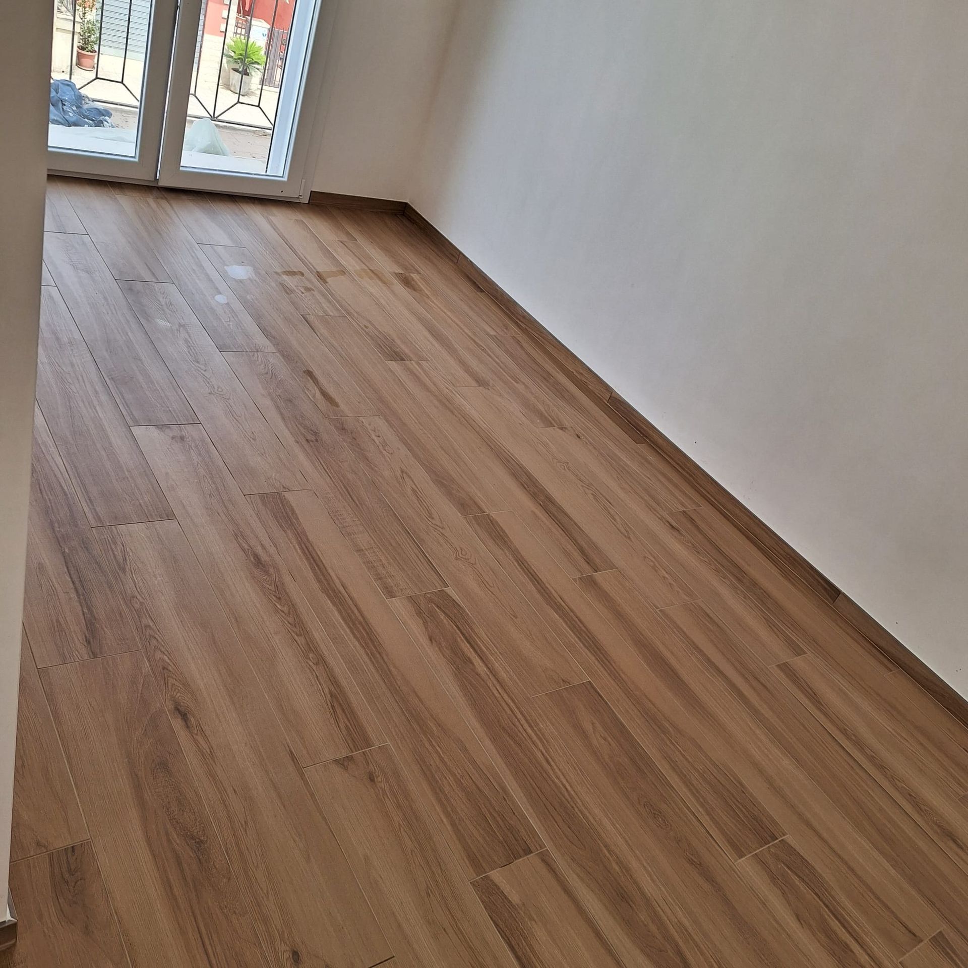Stanza vuota con pavimento in legno chiaro e porta a vetri in fondo.
