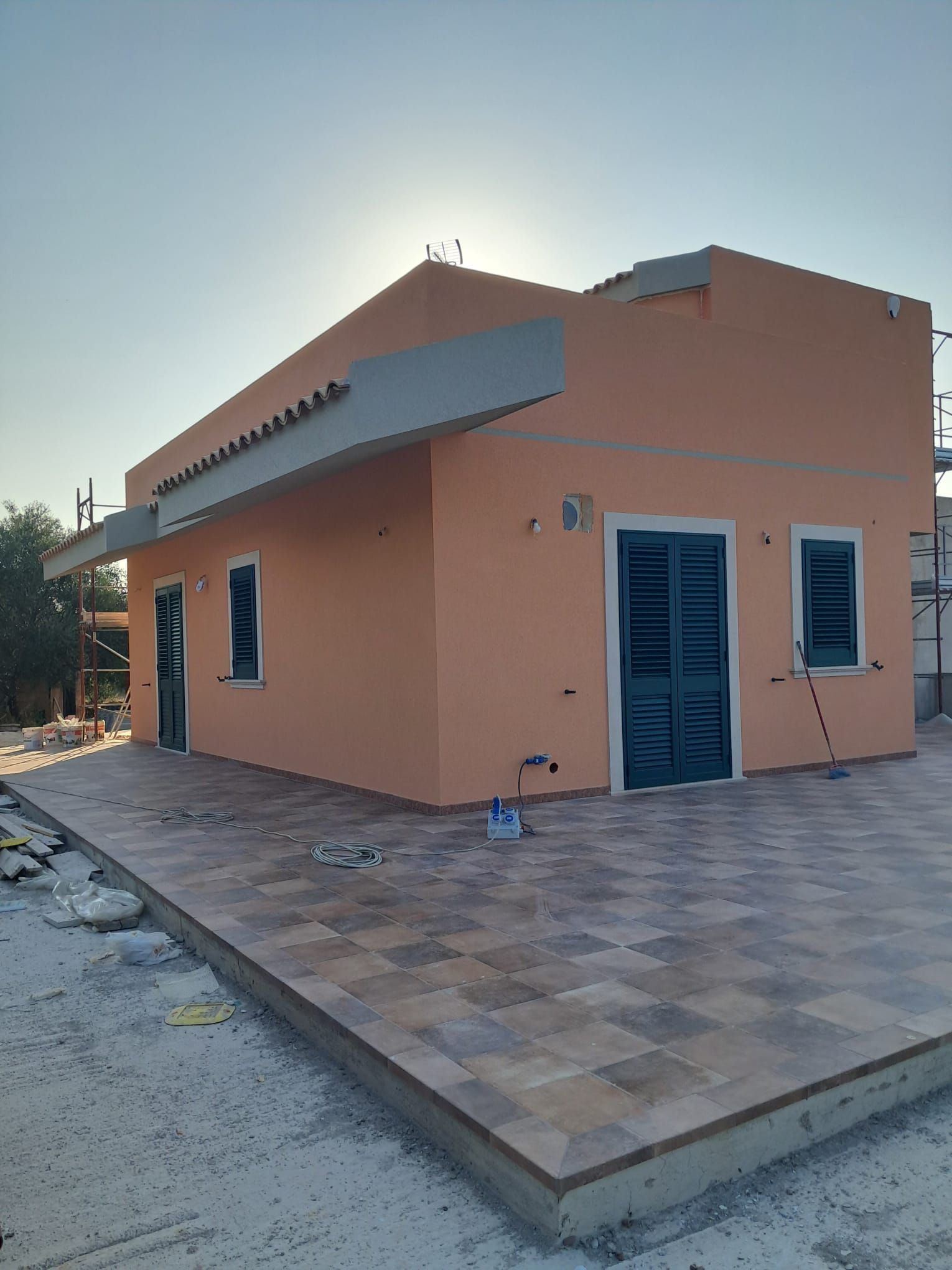 Casa color pesca a un solo piano con porte e finestre blu, vista da un patio anteriore piastrellato al tramonto.