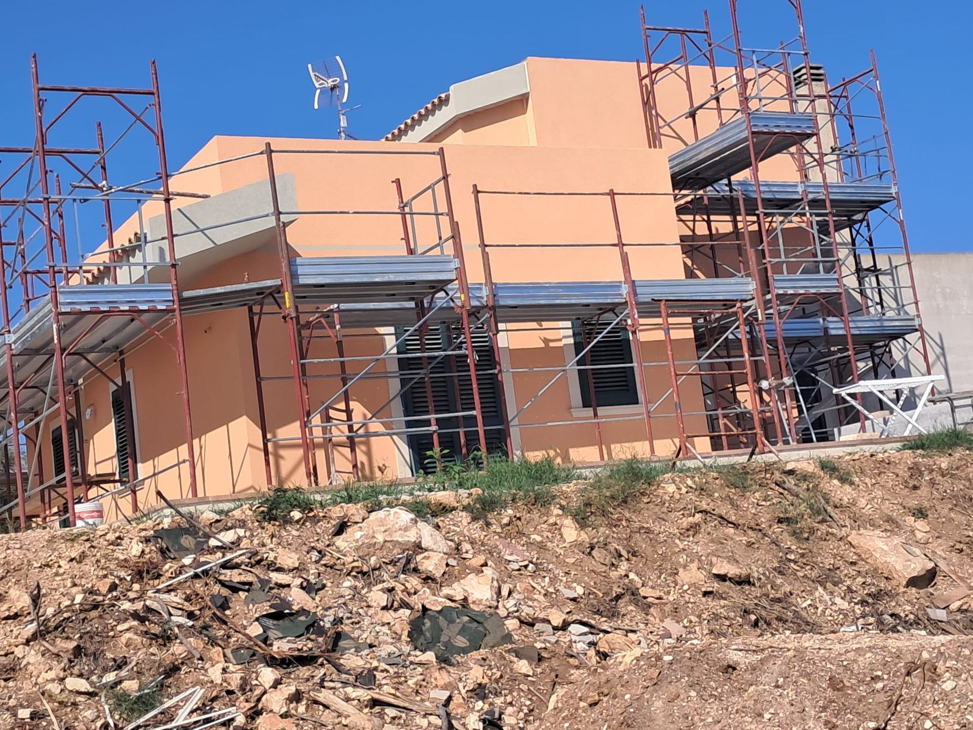 Casa a due piani in costruzione con impalcature su un lotto di terra sotto un cielo azzurro e limpido.