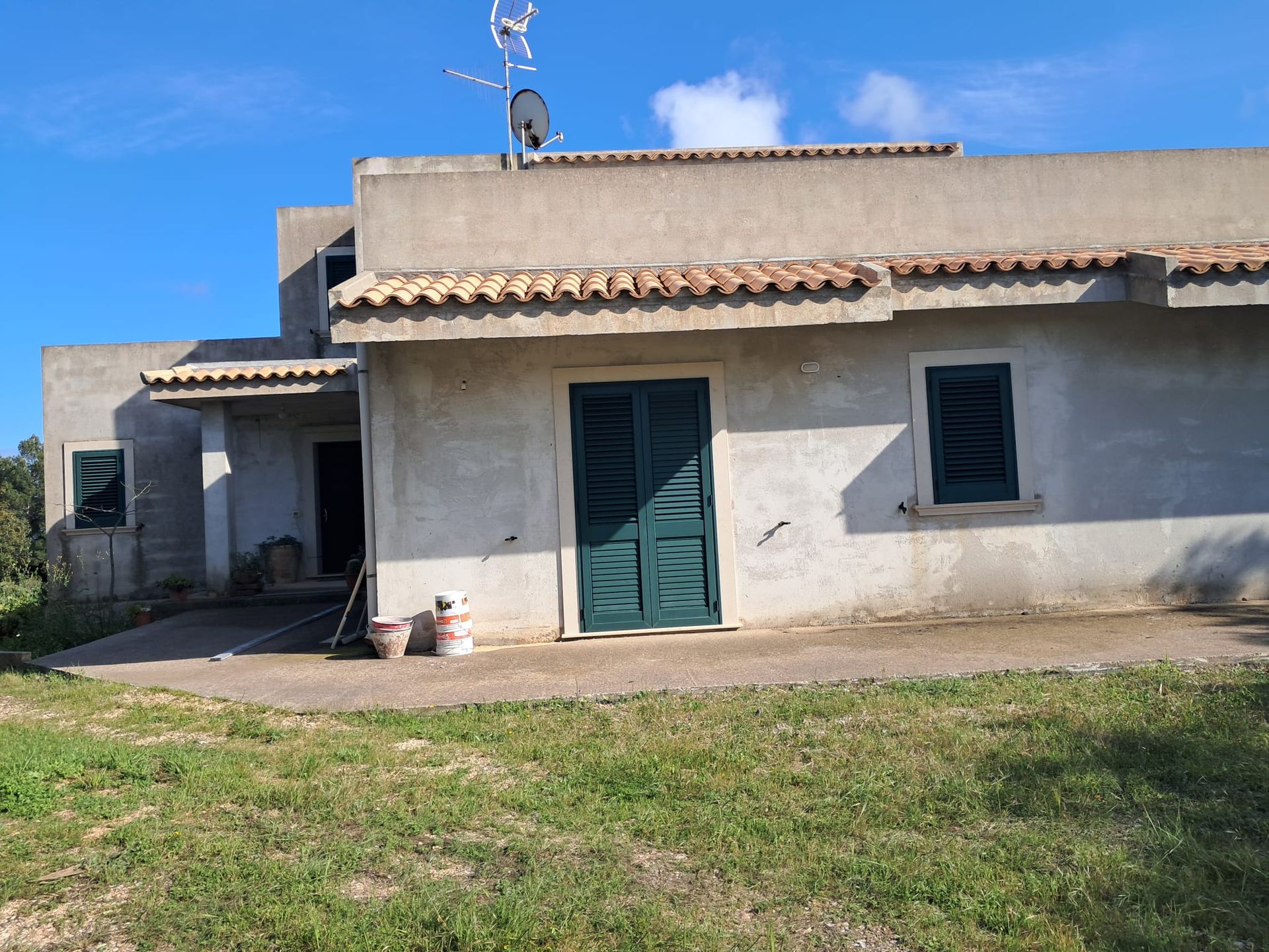 Casa singola in stucco con porta e finestre color verde acqua, situata dietro un prato sotto un cielo azzurro.