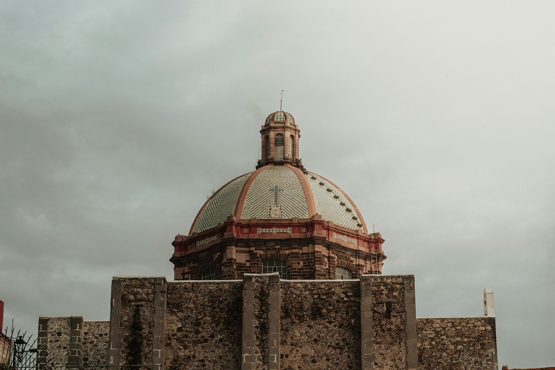 Cúpula de piedra y muralla de la fortaleza bajo un cielo nublado, con texto blanco superpuesto en el centro.