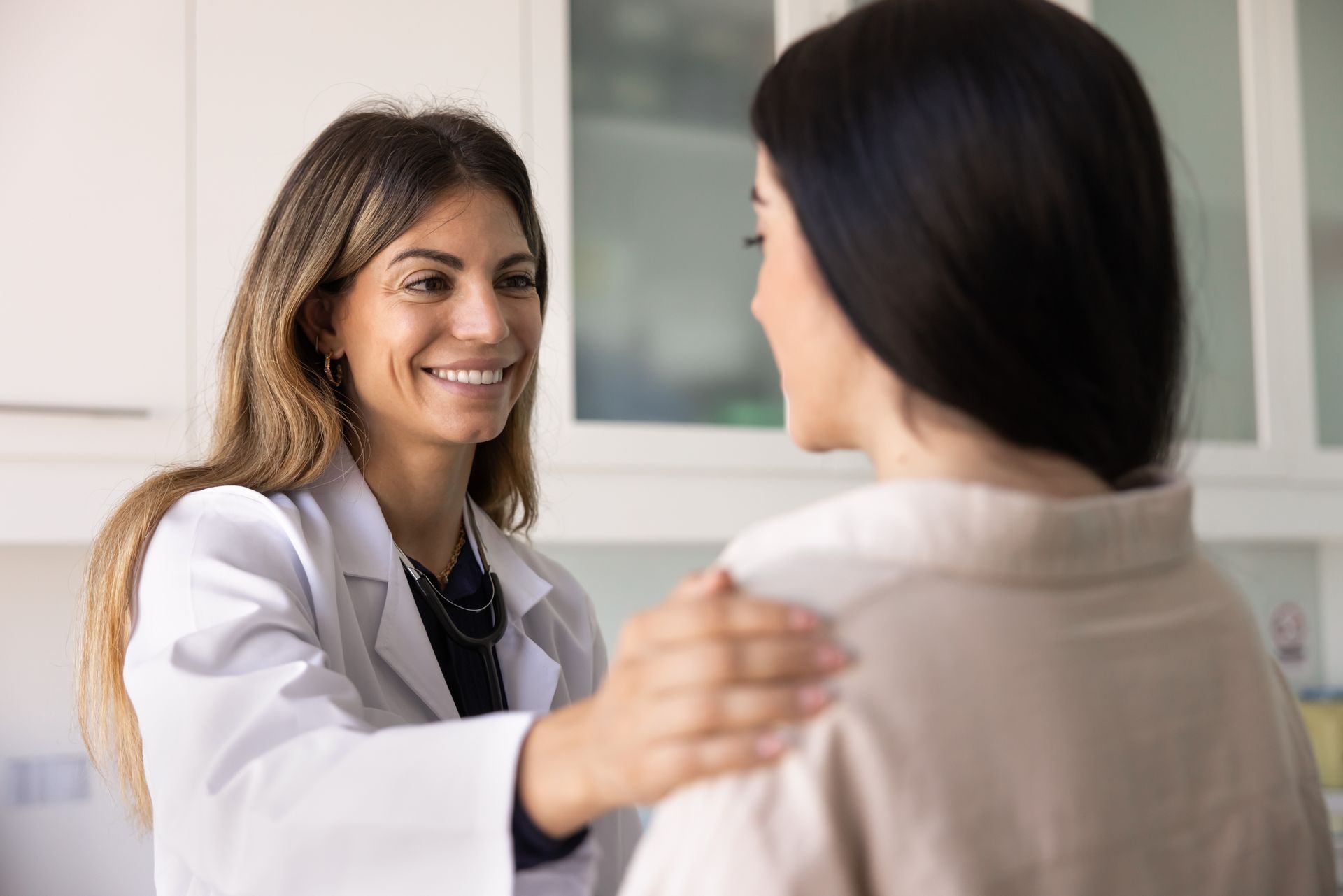 Smiling doctor comforts a patient with a hand on her shoulder at a women's health care clinic