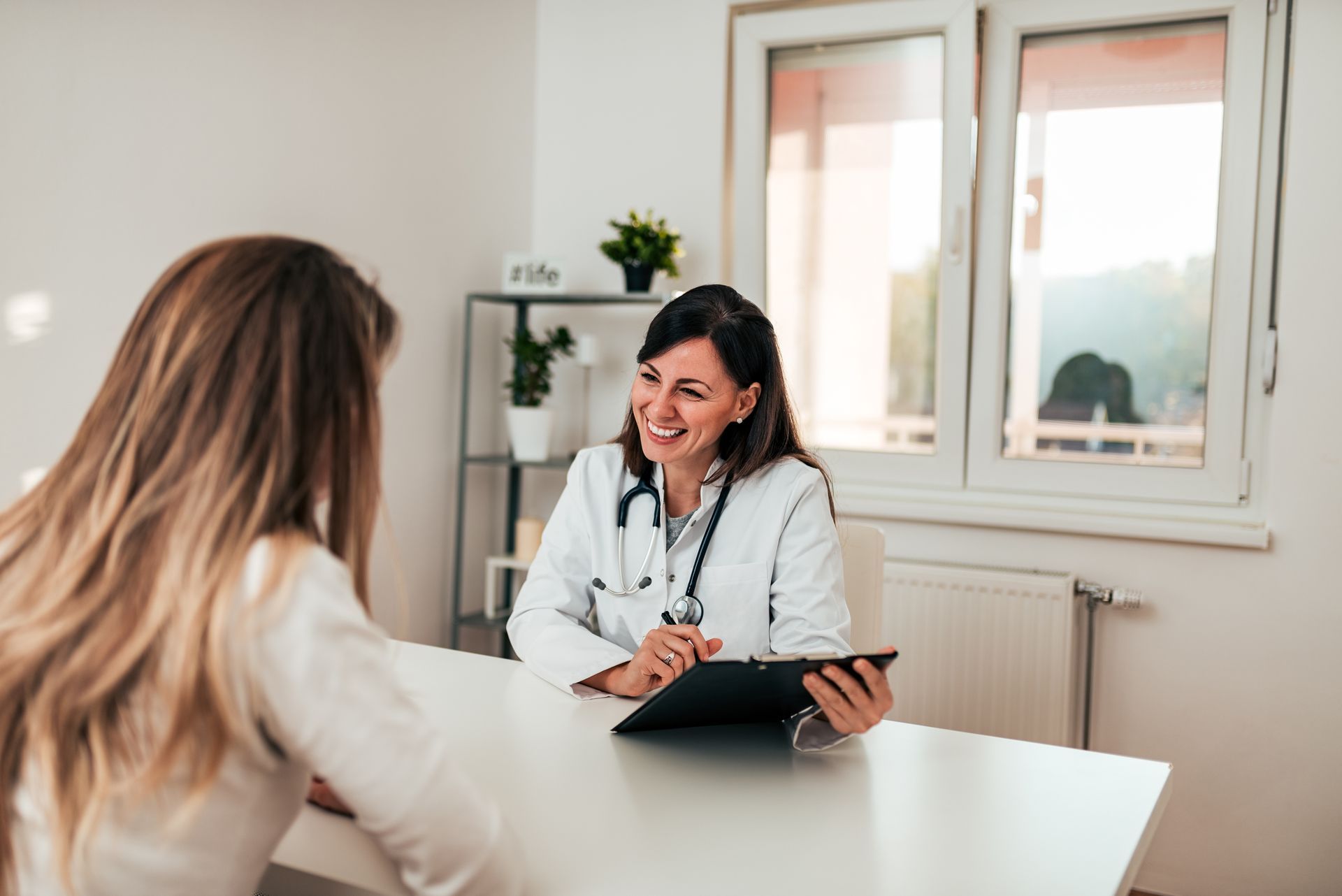 A healthcare provider consults with a patient at a desk in a bright, modern medical office.