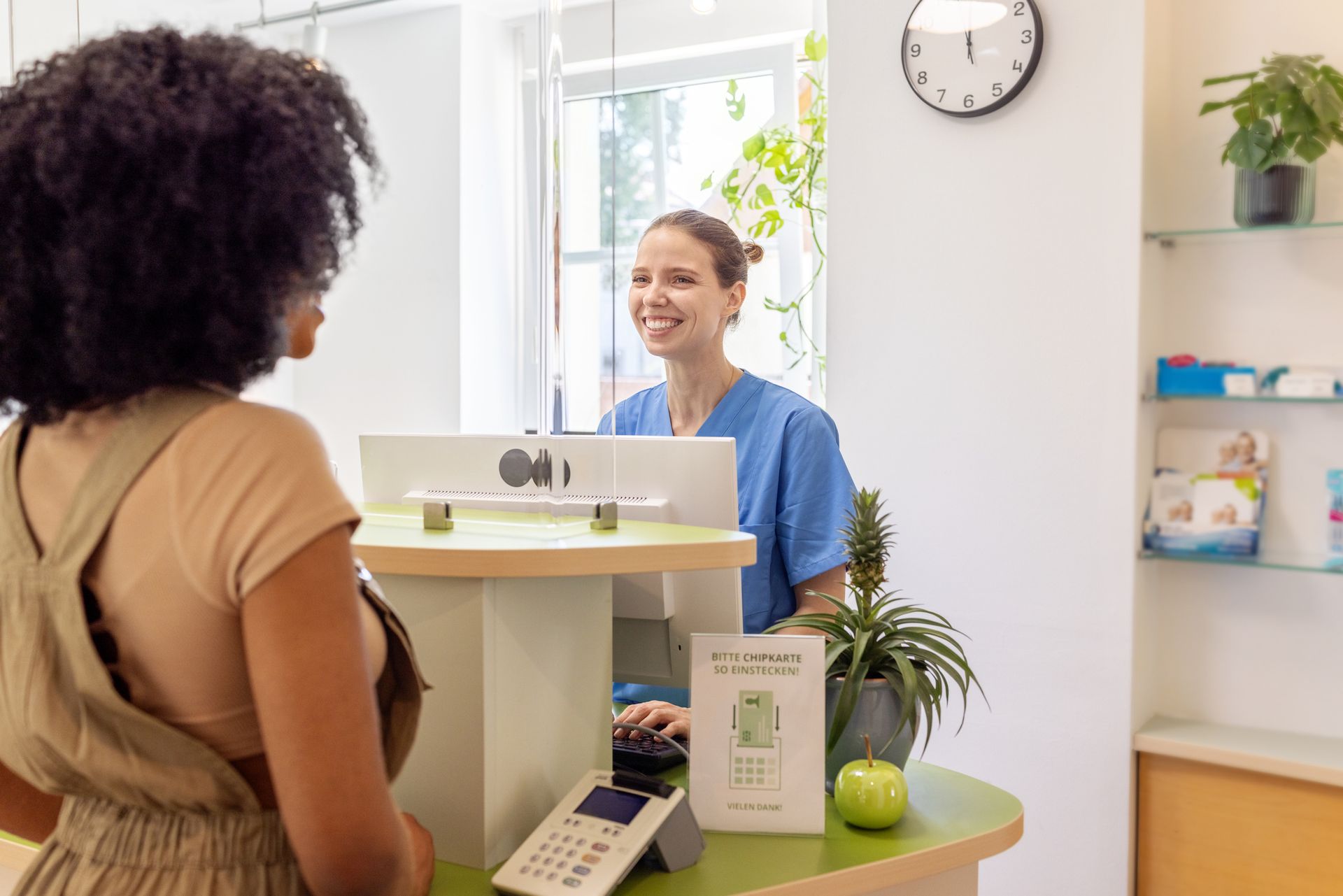 Receptionist greeting female patient with smile at modern women’s health clinic front desk.