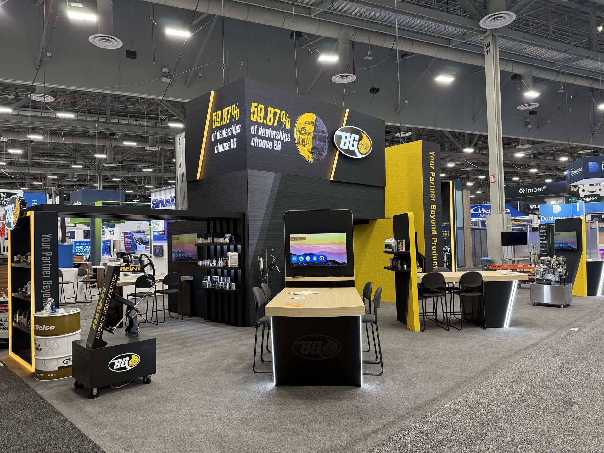 Black-and-yellow trade show booth with TV displays and counters in a large convention hall