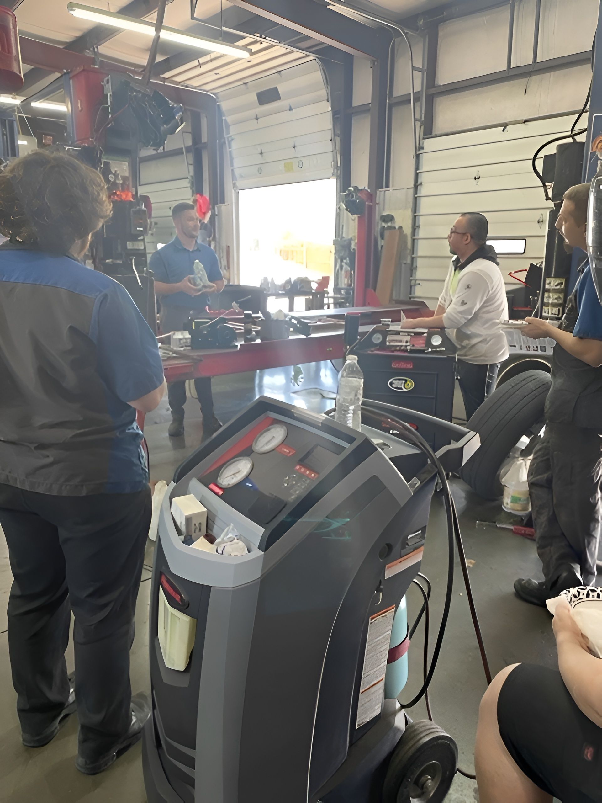 People gathered around a table in a garage or workshop, with a wheeled toolbox in the foreground.