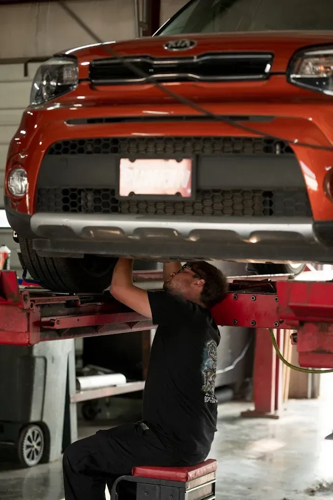 Mechanic working under a lifted orange SUV in a garage