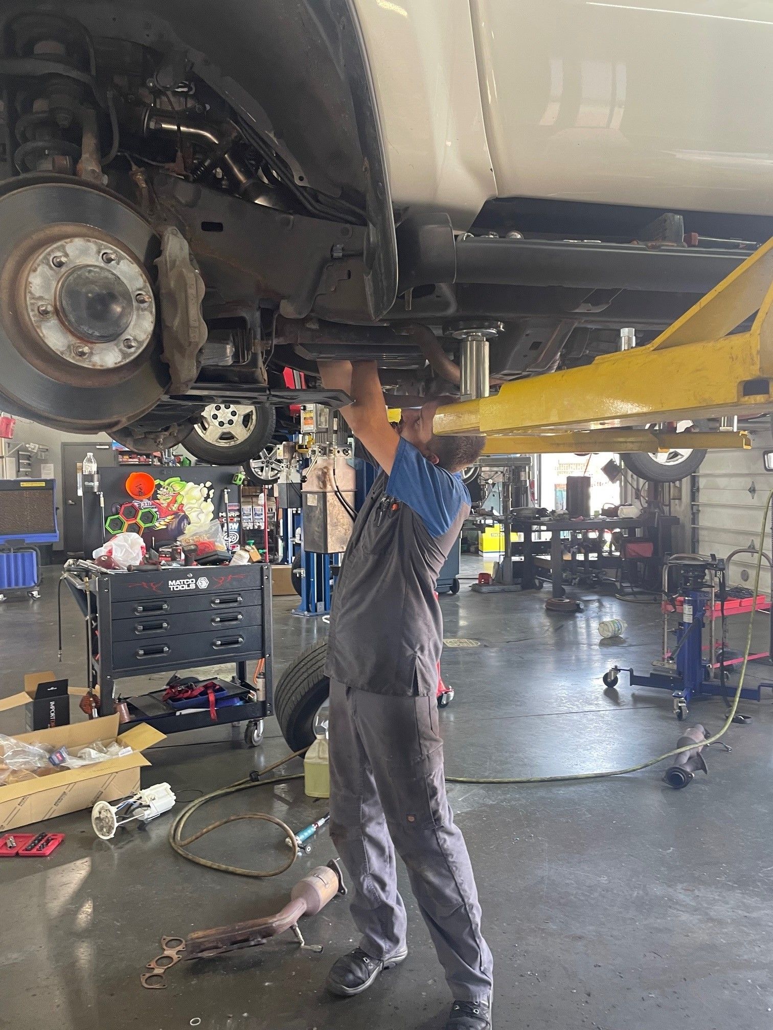 Mechanic working under a raised car in an auto repair shop, with tools and equipment nearby.