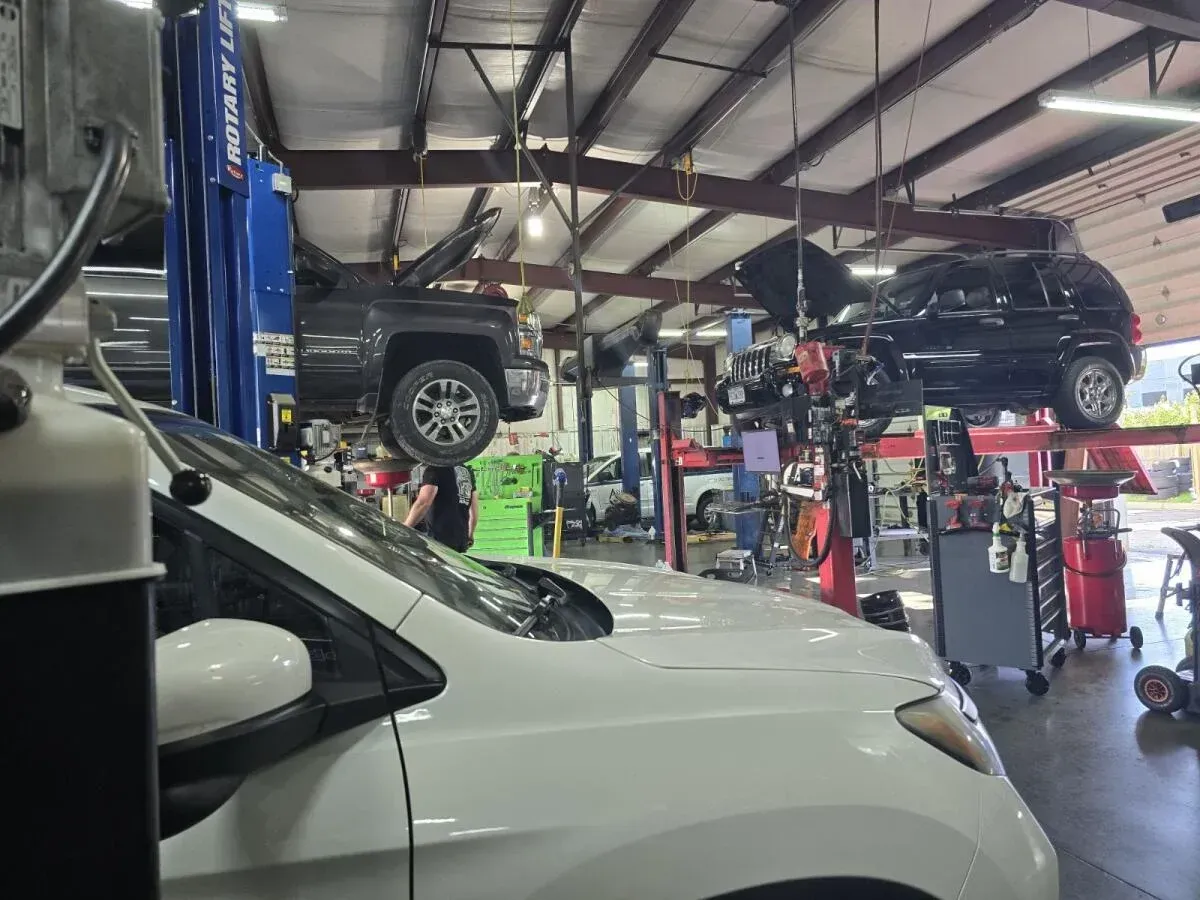 Auto repair shop with cars lifted on blue hydraulic lifts and a white car in the foreground