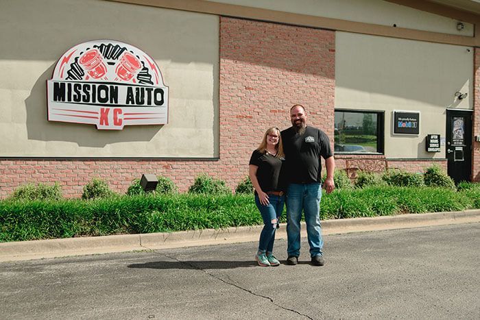 Two people standing outside Mission Auto and the office building sign.